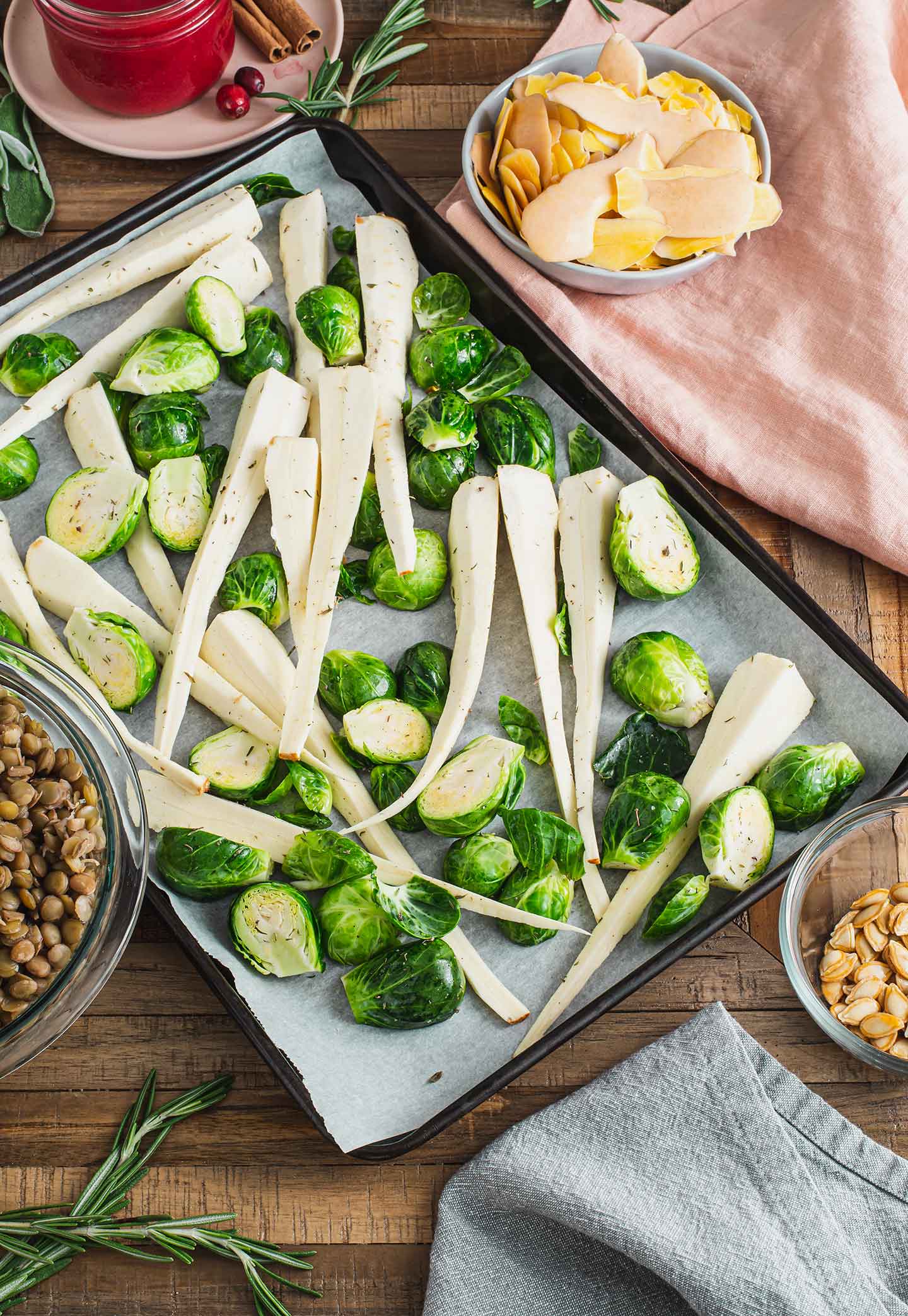 Top down view of sliced brussels sprouts and sliced parsnips on a baking tray lined with parchment paper.