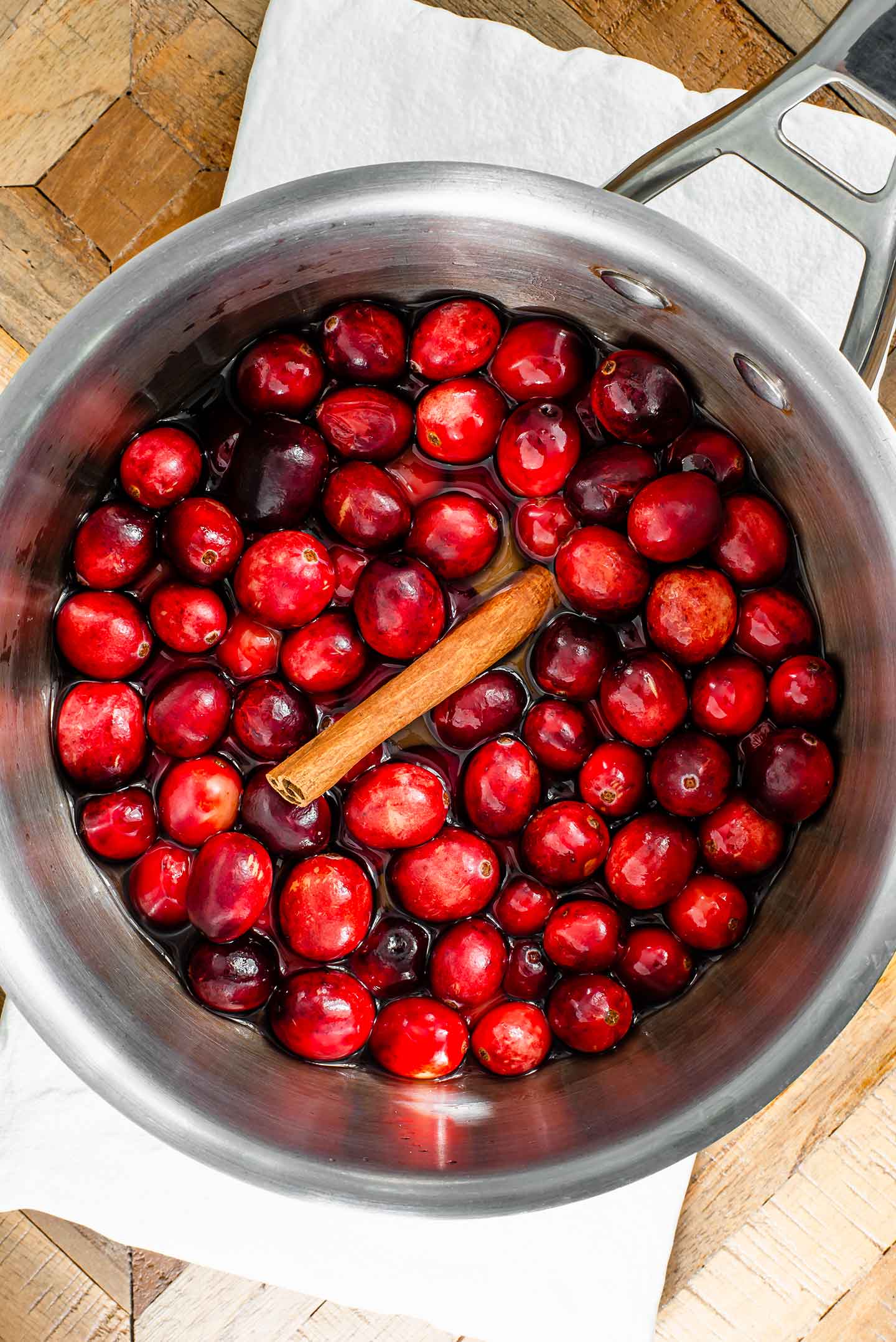 Top down view of whole cranberries in a pot of water with a cinnamon stick on top. 