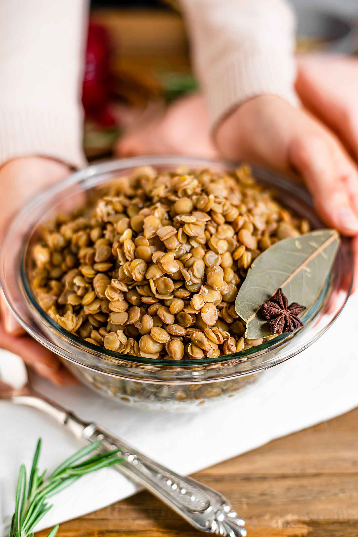 Side view of hands placing a bowl of cooked green lentils on a white tray. The lentils are garnished with a bay leaf and star anise. 
