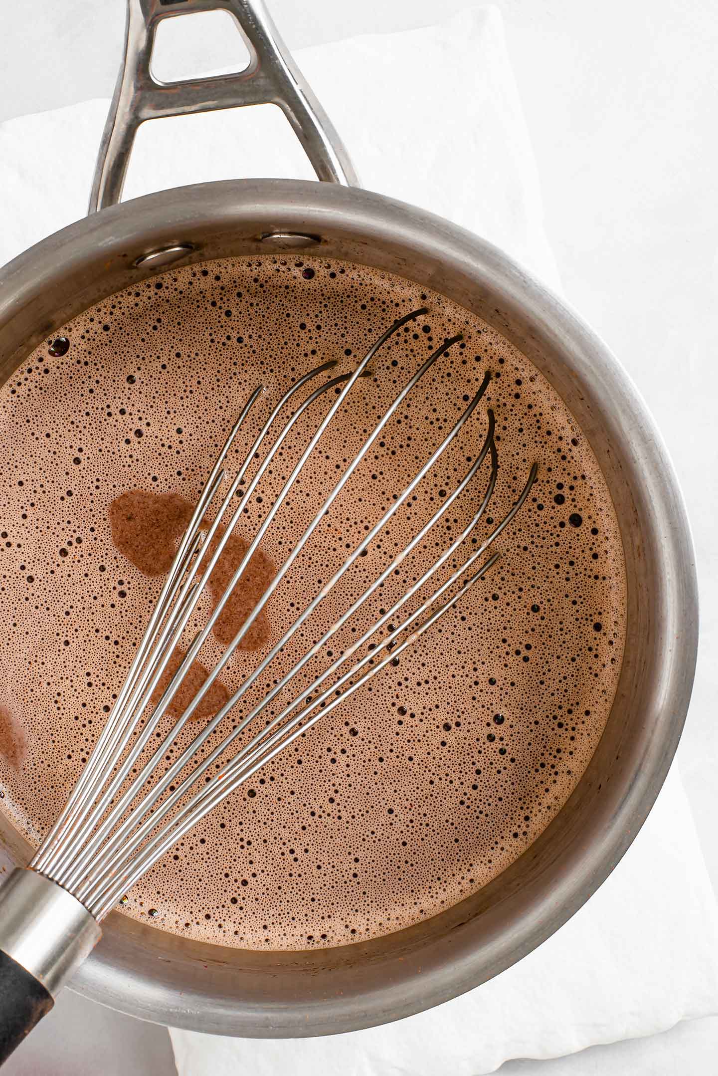 Top down view of hot chocolate in a pot with a whisk.