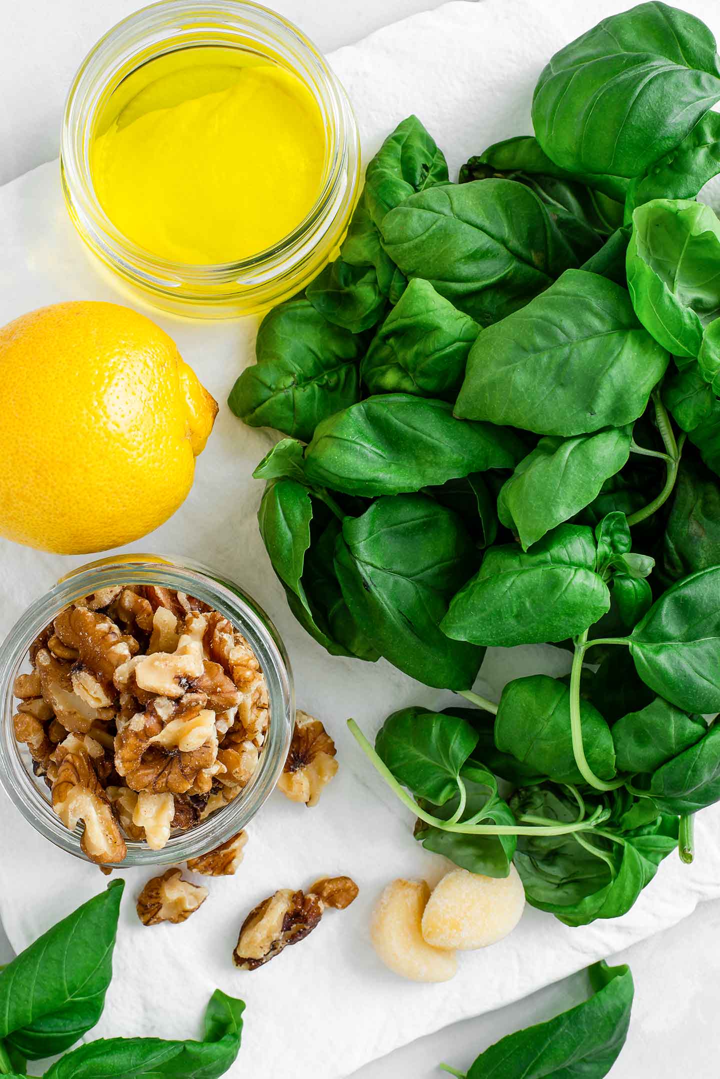 Top down view of basil leaves, walnuts, lemon juice, garlic, and olive oil.