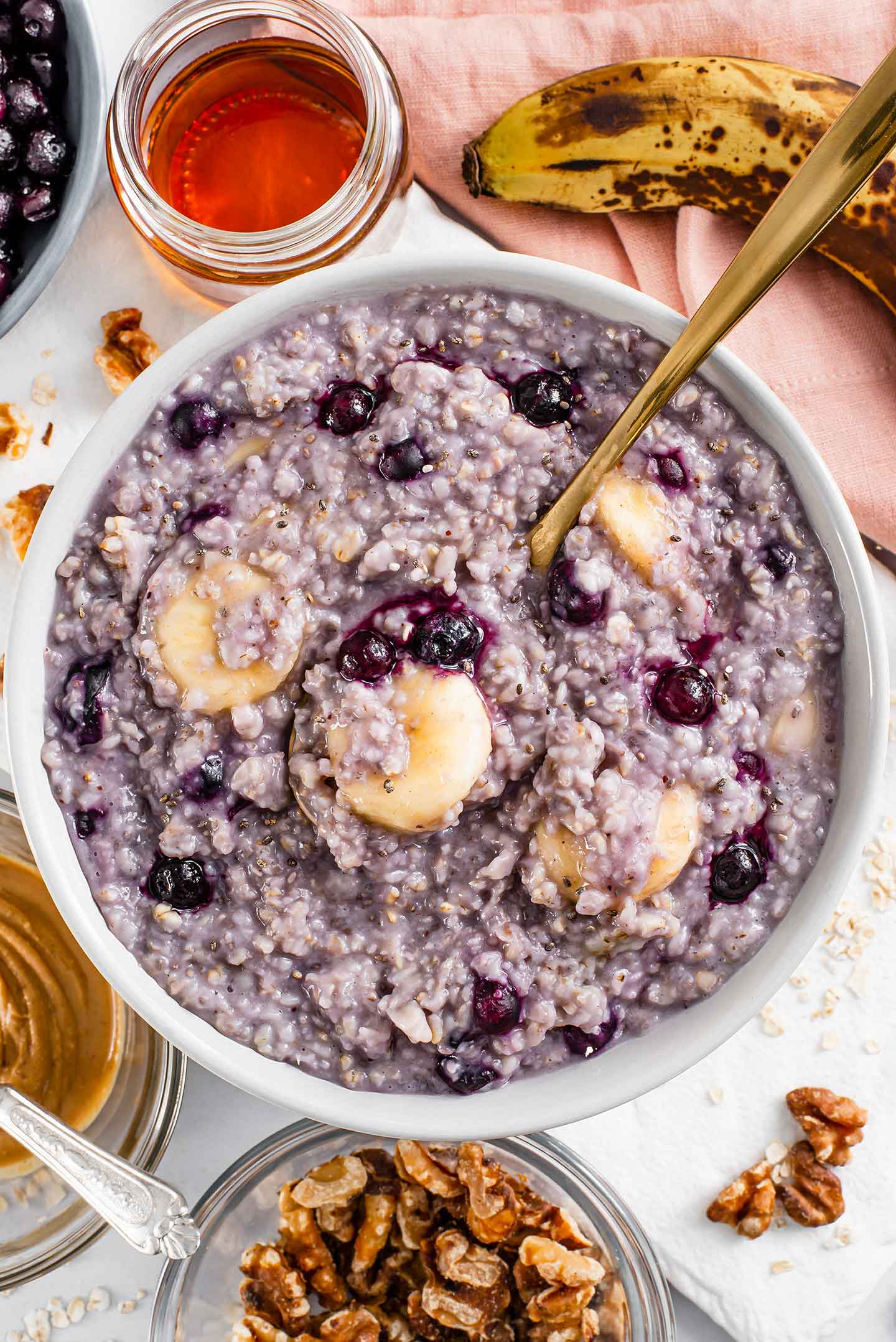 Top down view of quick blueberry banana oatmeal in a bowl. A spoon rests in the middle with soft slices of banana and heated blueberries melting into the purple tinged oats.