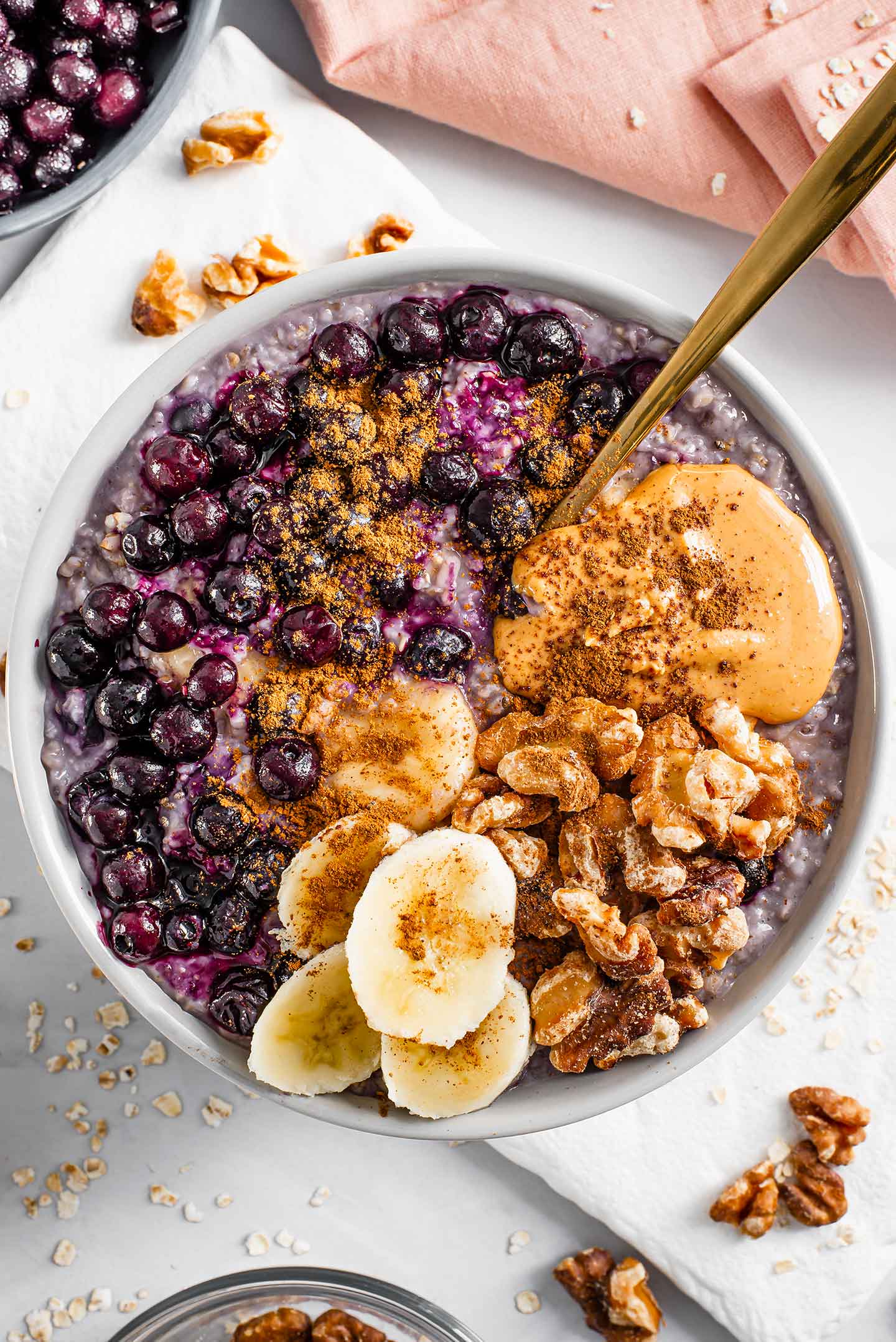 Top down view of blueberry banana oats in a bowl with walnuts, extra blueberries and a pink napkin just visible in the frame.