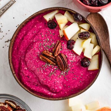 A bright pink apple beet smoothie bowl topped with diced apple, toasted pecans, chia seeds, and dried cranberries.