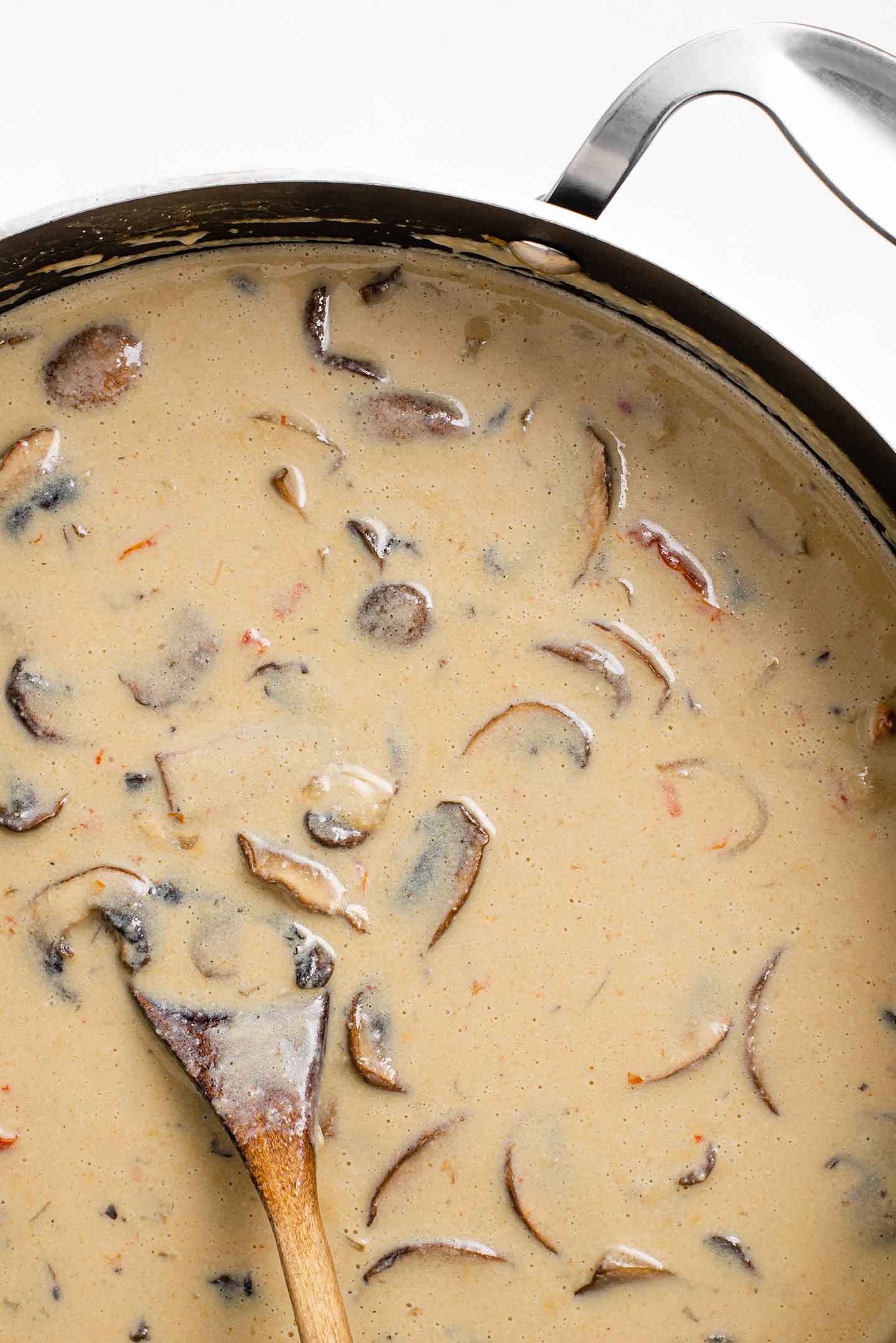 Top down view of creamy speedy stroganoff in a saucepan before the noodles are added. The sauce is thick, a light brown colour from the sour cream and the dark broth, and it's full of mushrooms and sun-dried tomato.