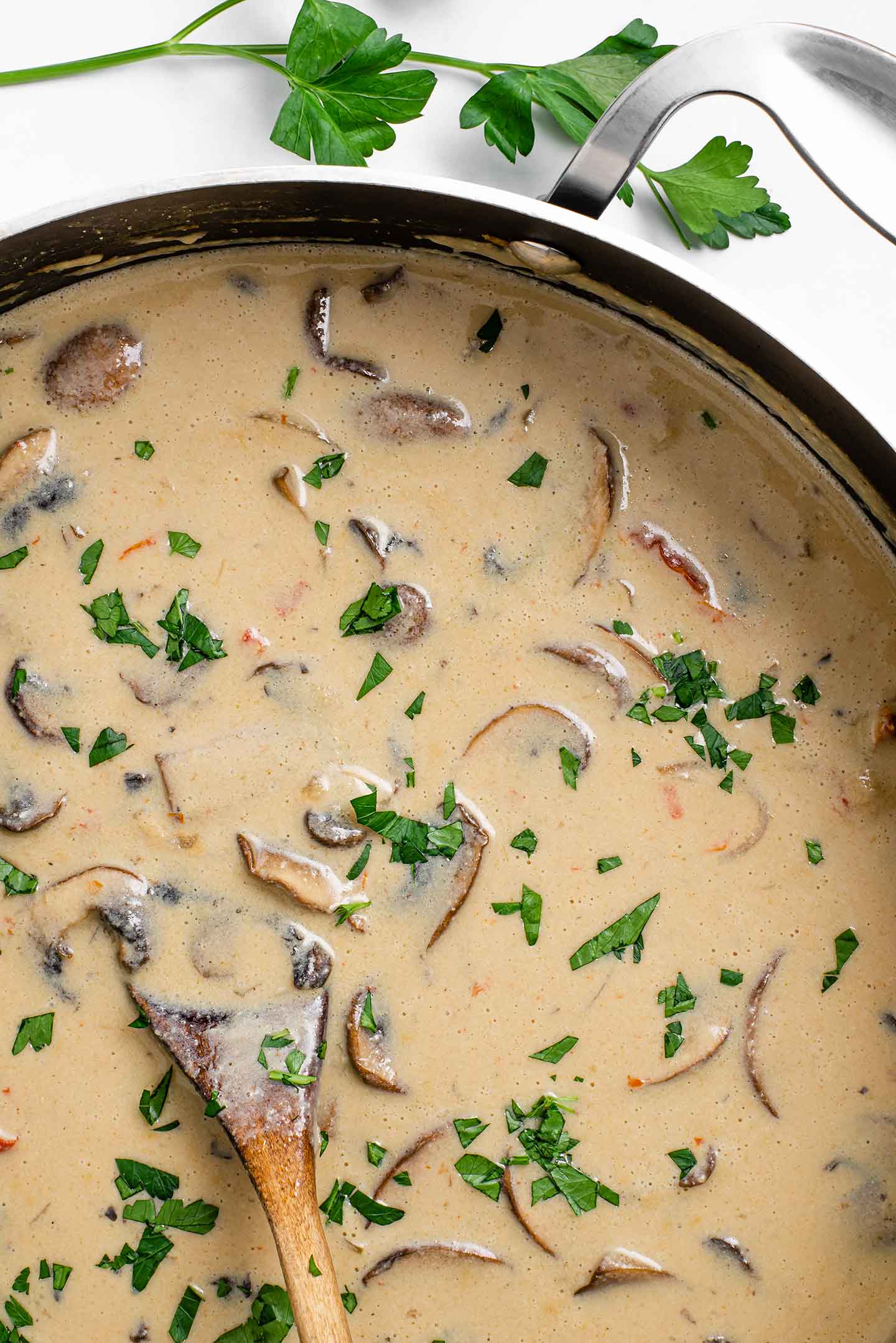 Top down view of the creamy, cost saving stroganoff in a saucepan with a wooden spoon. It is garnished with fresh parsley.
