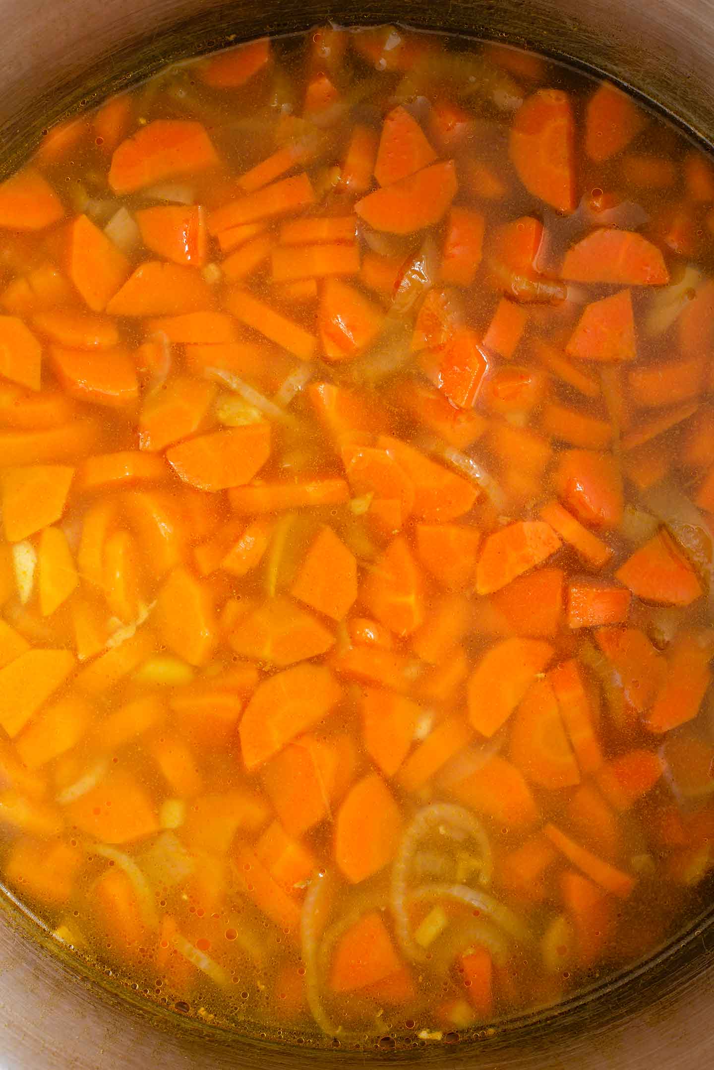 Top down view of carrot ginger soup before it is blended. The diced carrots and onion float in the veggie broth.