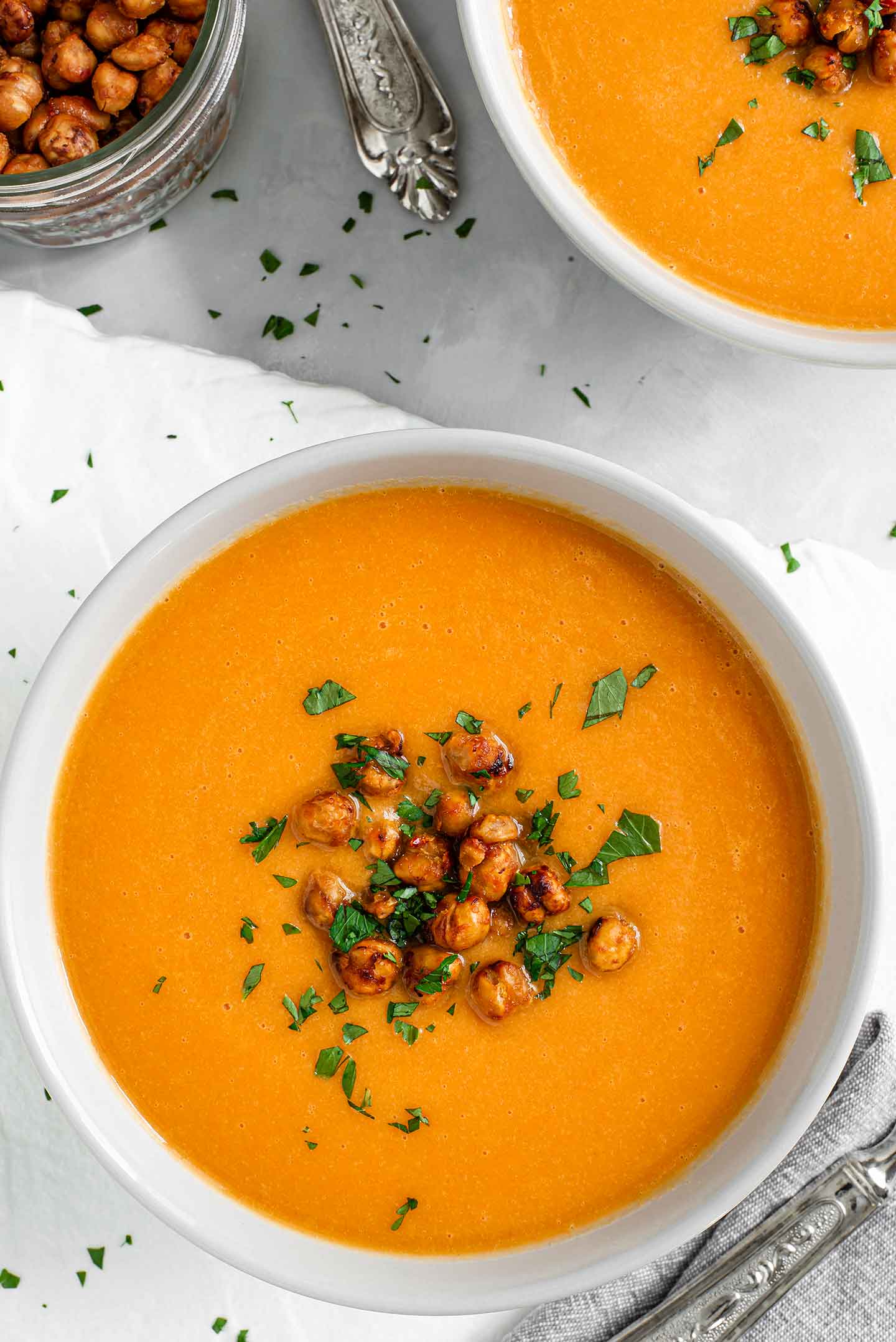 Top down view of two bowls of creamy carrot ginger soup topped with roasted chickpeas and parsley.