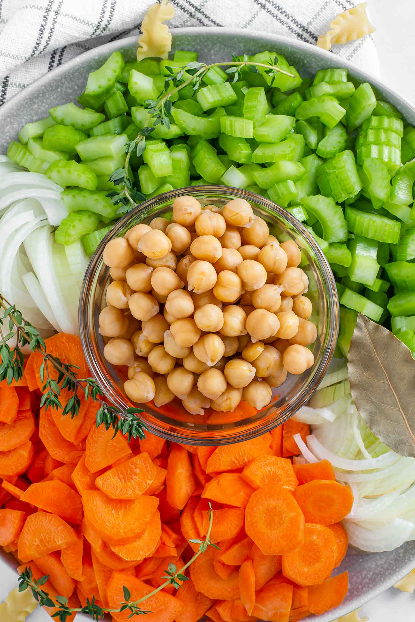 Top down view of chickpeas in a small glass bowl with chopped celery, chopped carrots, and sliced onion displayed around.