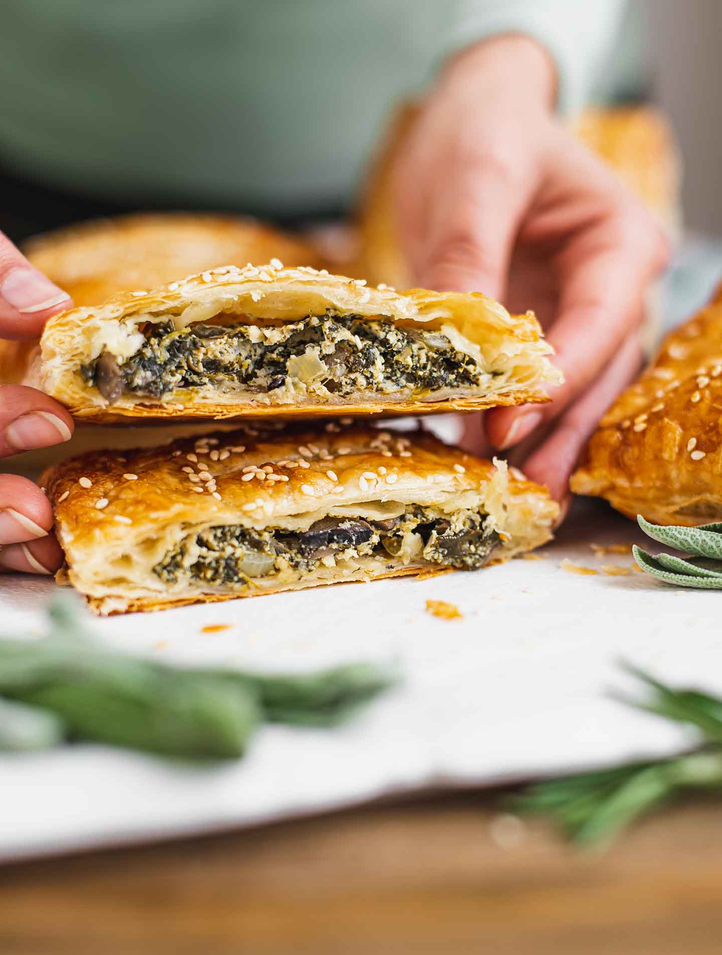 Side view of a puff pastry pocket sliced in half and stacked one half on the other. The warm spinach, mushroom, tofu ricotta mixture is visible within the flaky pastry.