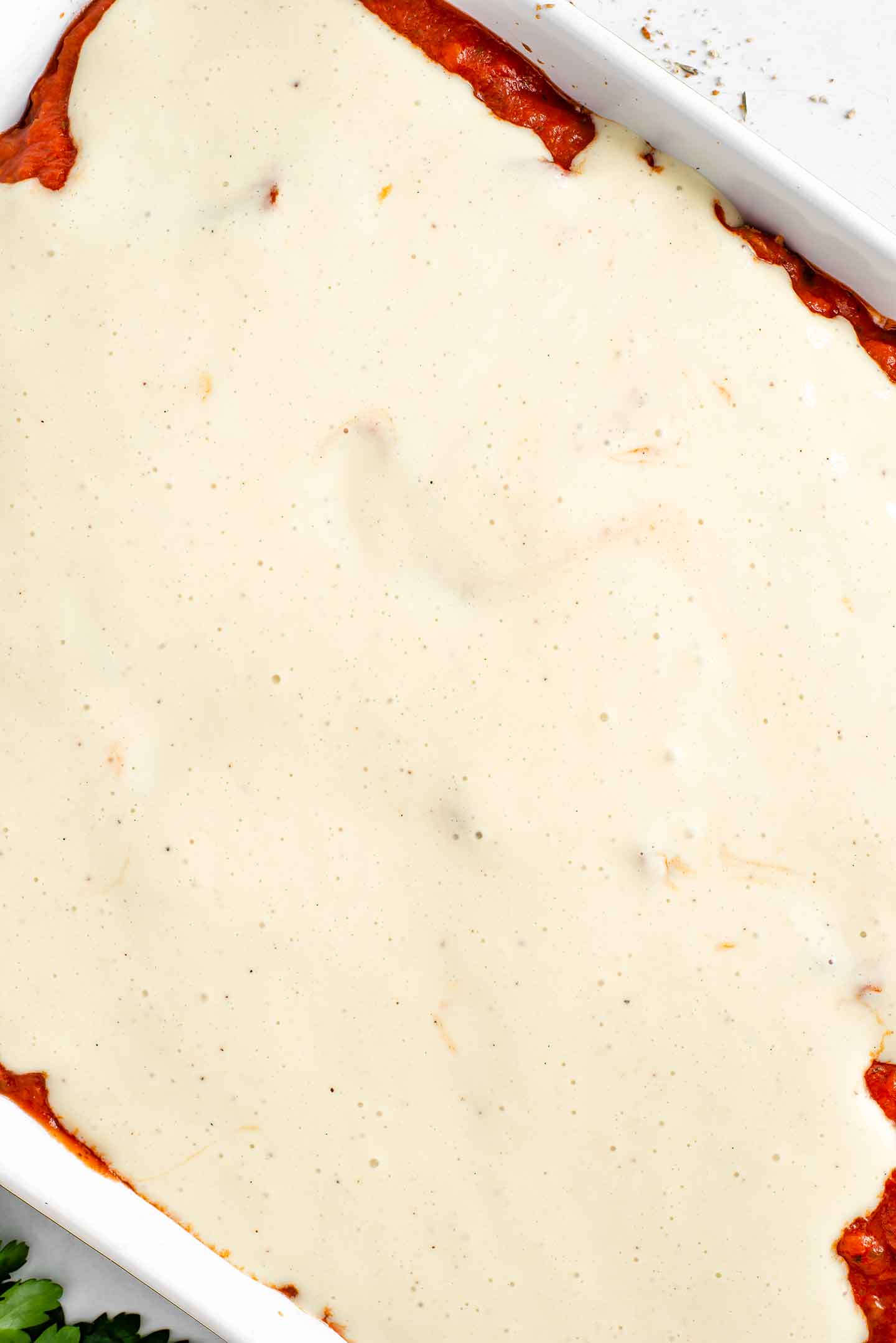 Top down view of white, cheesy bechamel sauce covering the top of the eggplant "parm" before going in the oven.