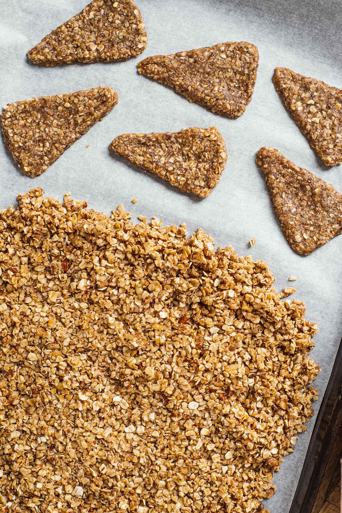 Top down view of the granola and pie shaped cookies on a parchment lined baking sheet.