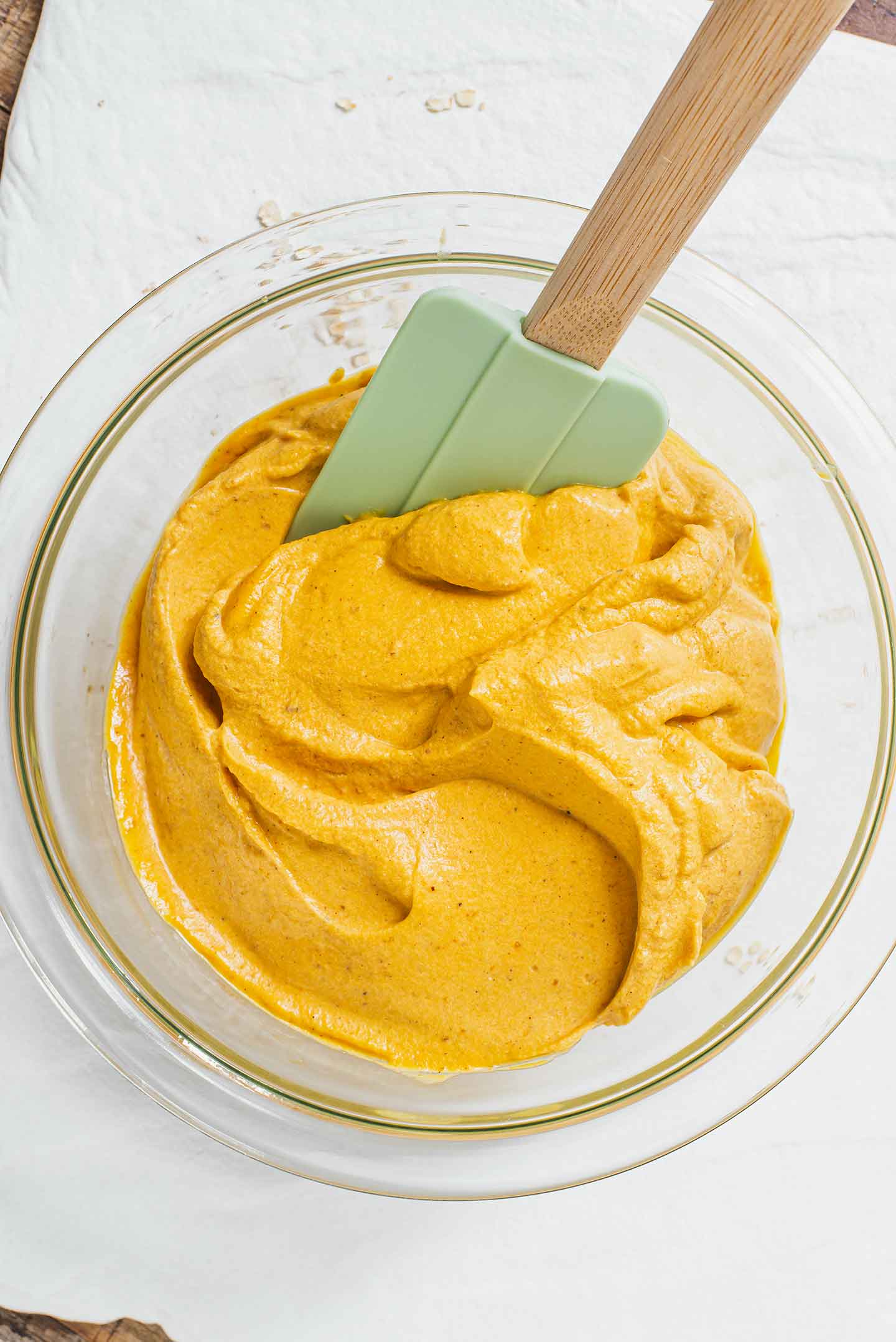 Top down view of creamy and thick pumpkin mousse in a glass bowl with a rubber spatula swirling the mixture.