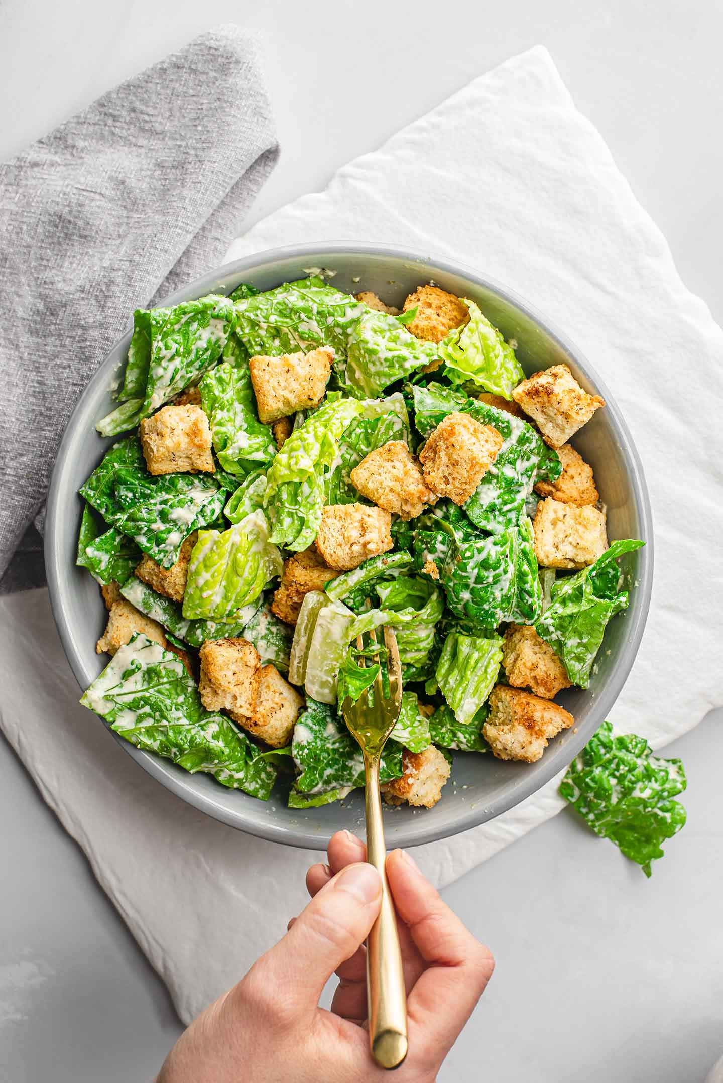 Top down view of romaine lettuce in a bowl covered in zingy caesar dressing and homemade croutons with a fork digging in.