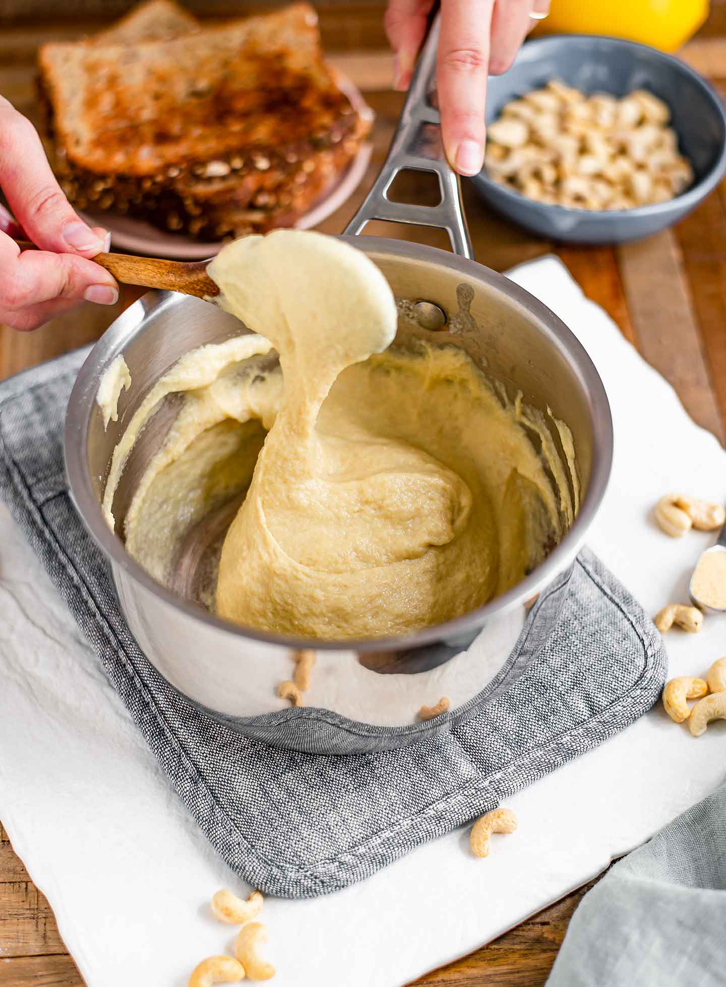 Top down view of a cheesy ball that has formed in a metal pot. A wooden spoon stretches the cheese upwards.