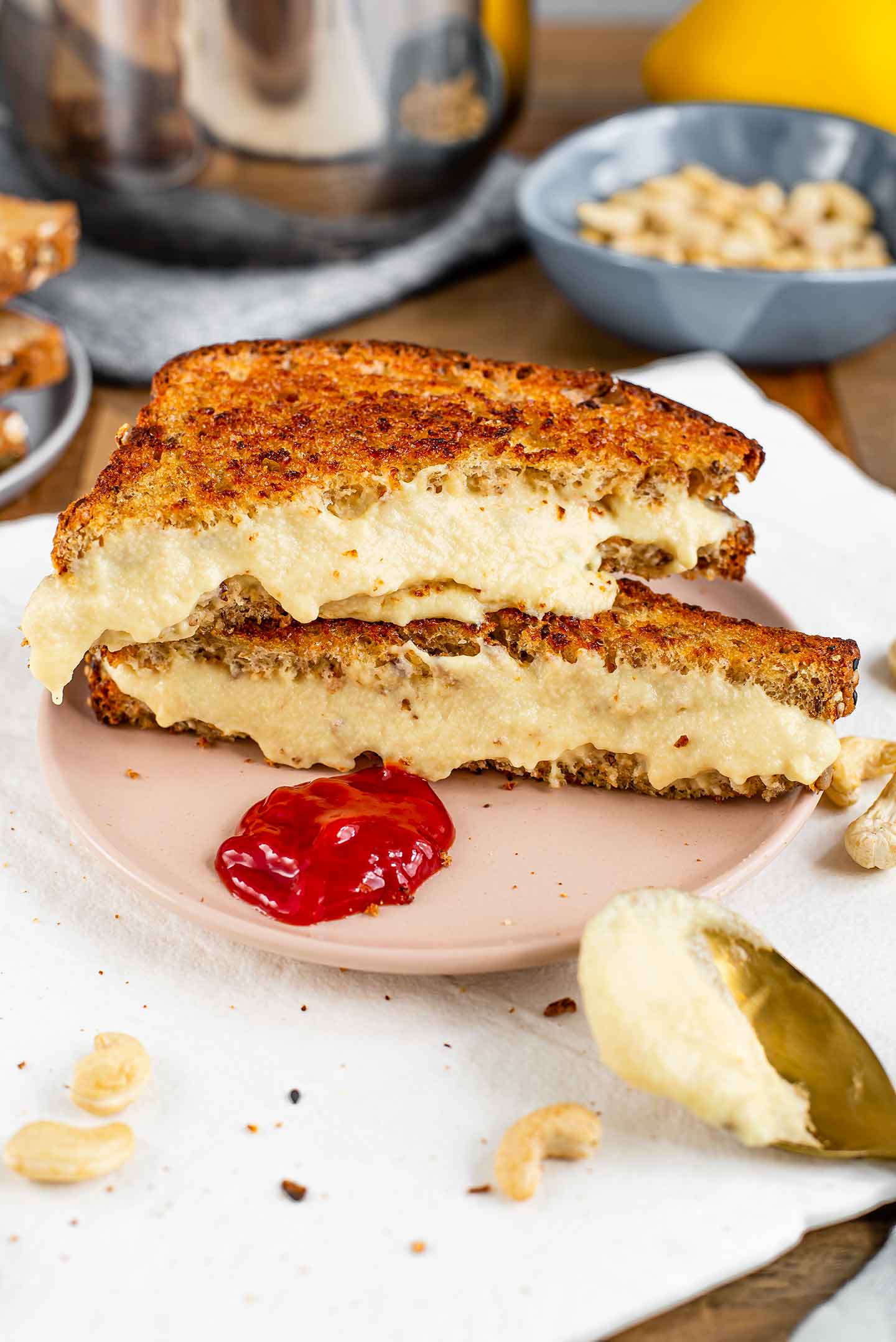 Side view of two halves of a grilled cheese sandwich stacked one on the other. It is filled with a thick and melty cashew mozzarella. A dollop of ketchup rests on the plate in front of the sandwich.