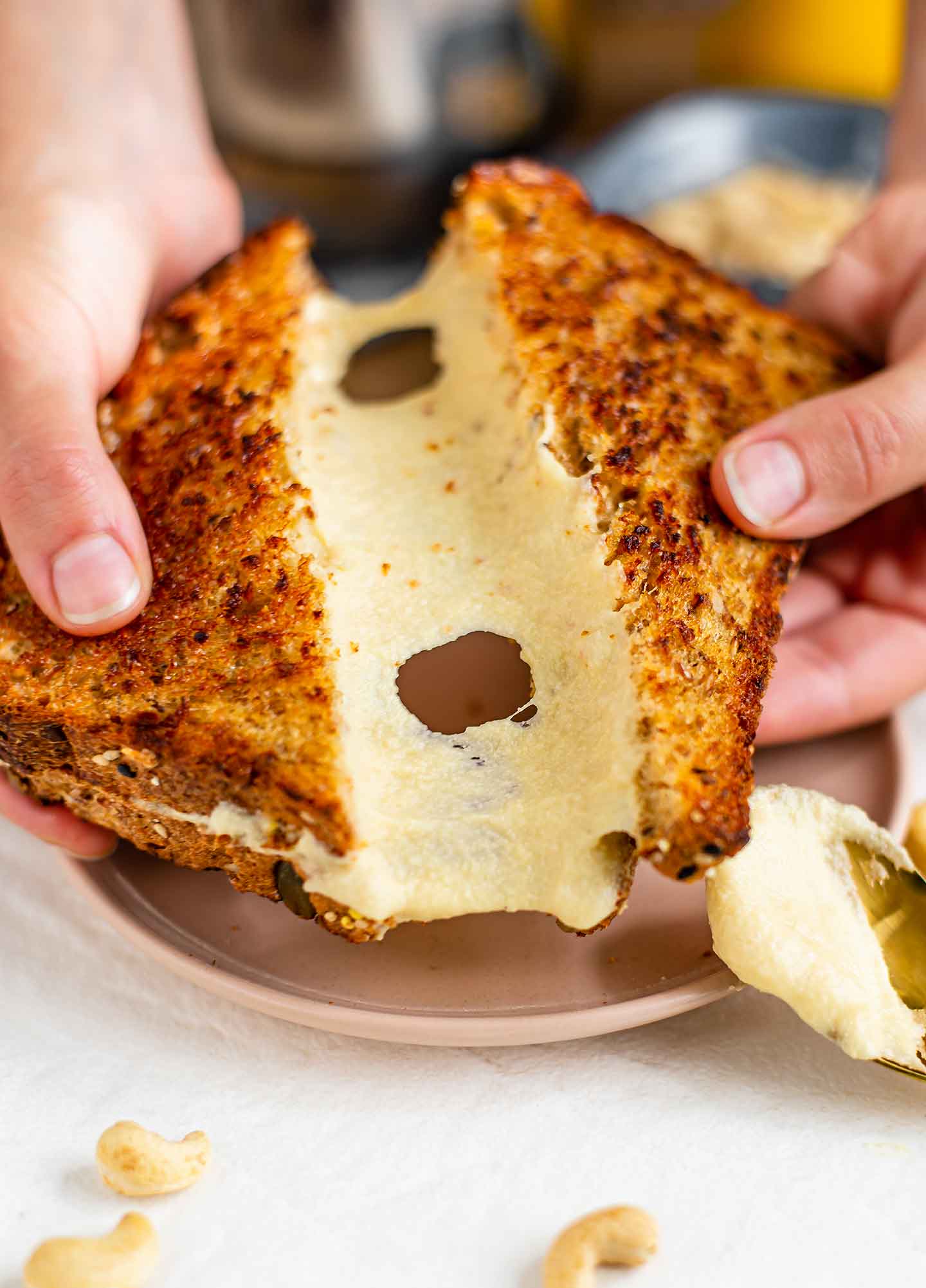 Side view of hands pulling two halves of a grilled cheese sandwich apart. The cheese is a stretchy cashew mozzarella that stretches dramatically between the two halves.