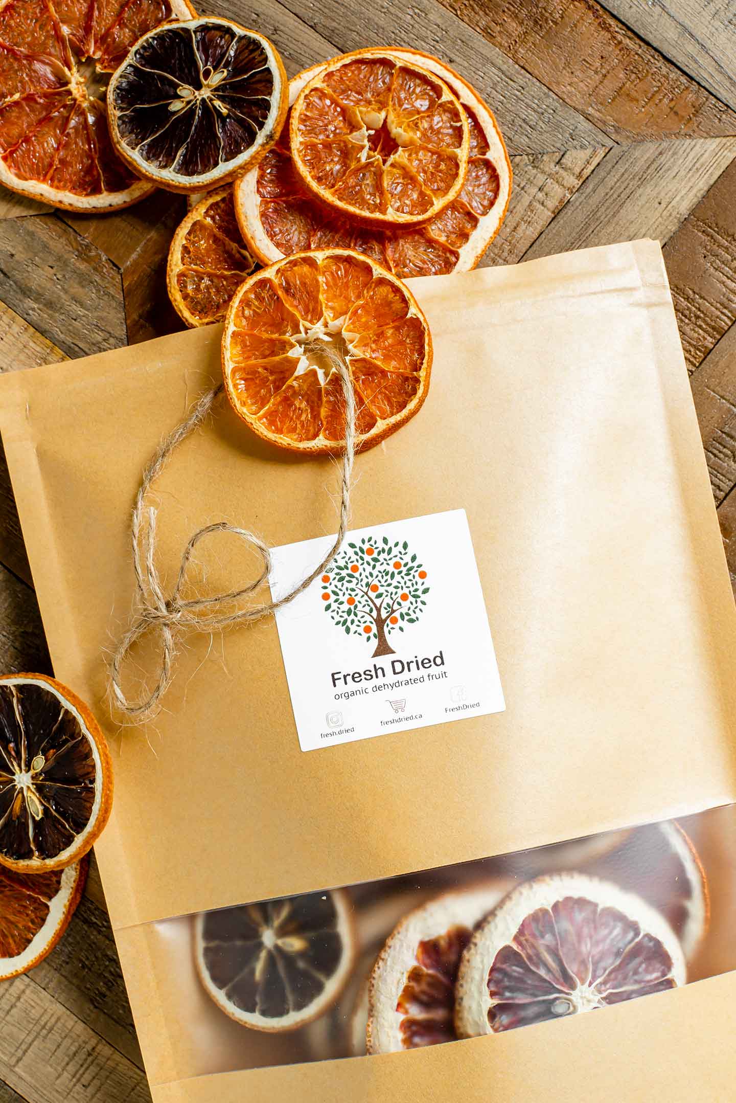 Top down view of a paper pouch with a sticker from the company "Fresh Dried". Dried slices of organic citrus fruit spill out of the bag and one has a piece of twine threaded through the centre to create a hanging decoration.