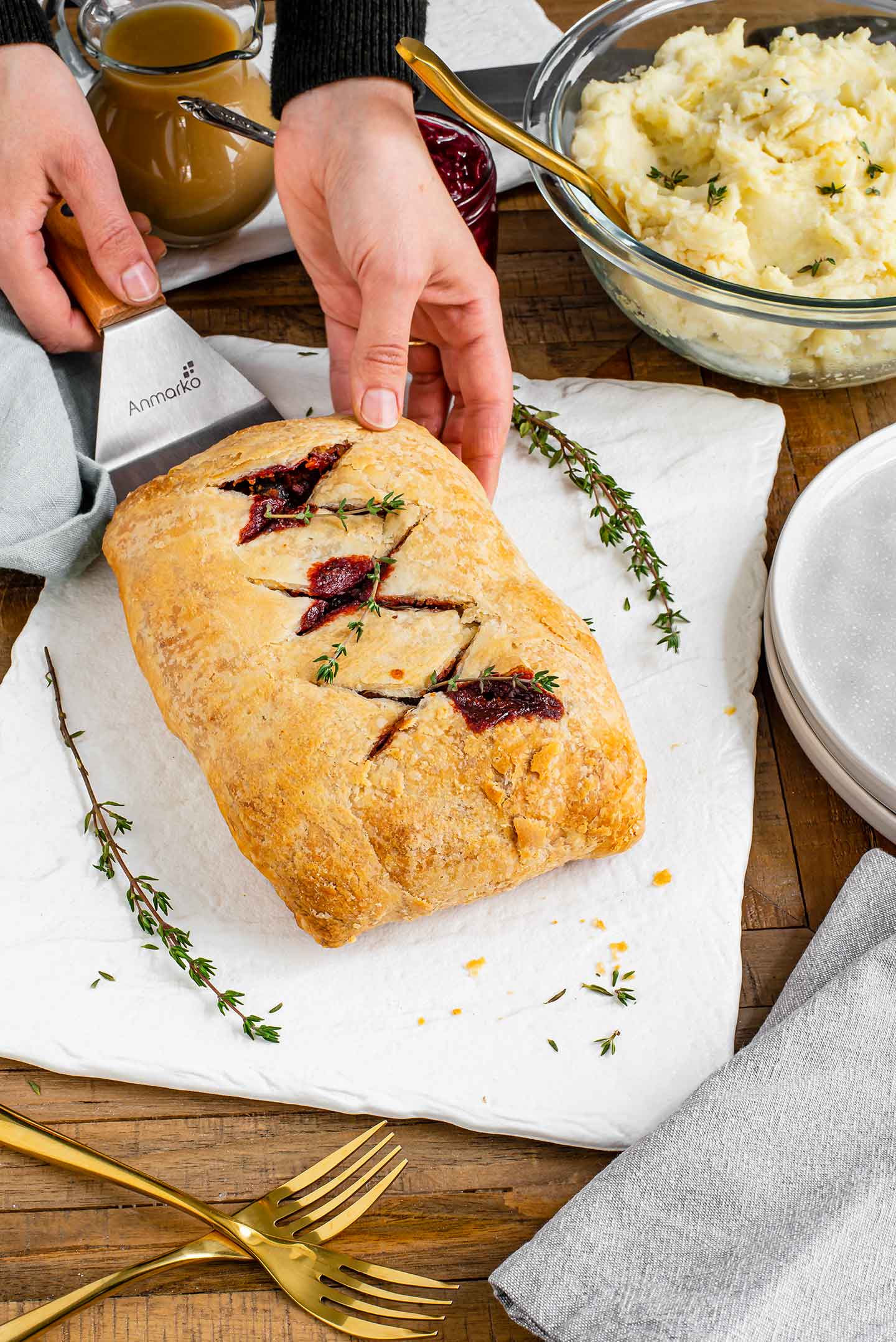 Hands slide a golden beet wellington off a large spatula onto a white tray.