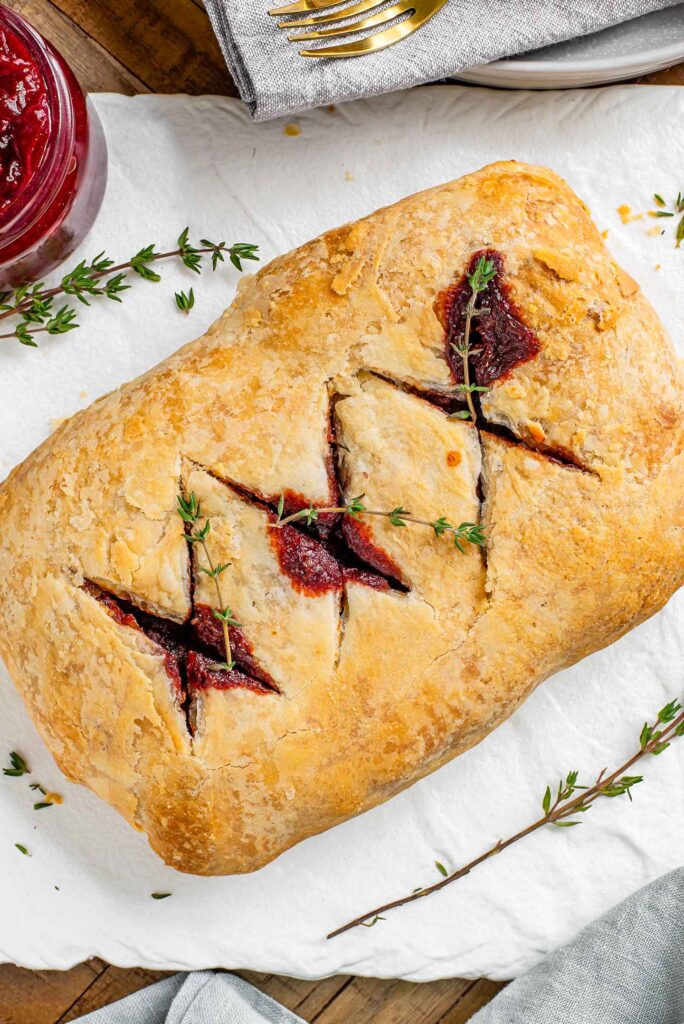 Top down view of a vegan beet wellington. The pastry is golden and the juices from the beet wellington stain the criss cross pattern in top. Sprigs of thyme garnish.