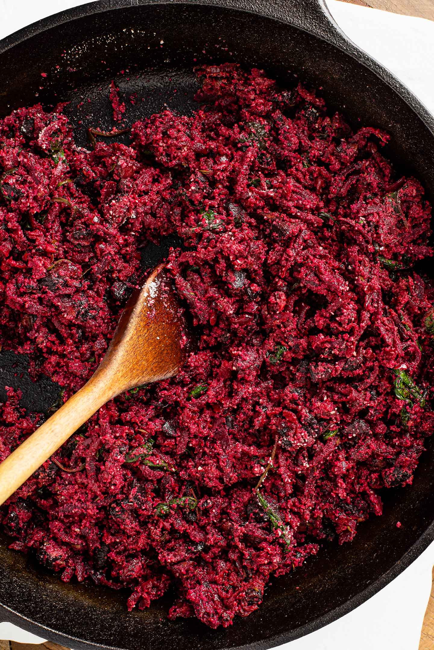 Top down view of the wellington filling in a cast iron pan with a wooden spoon resting in the deep red coloured mixture.