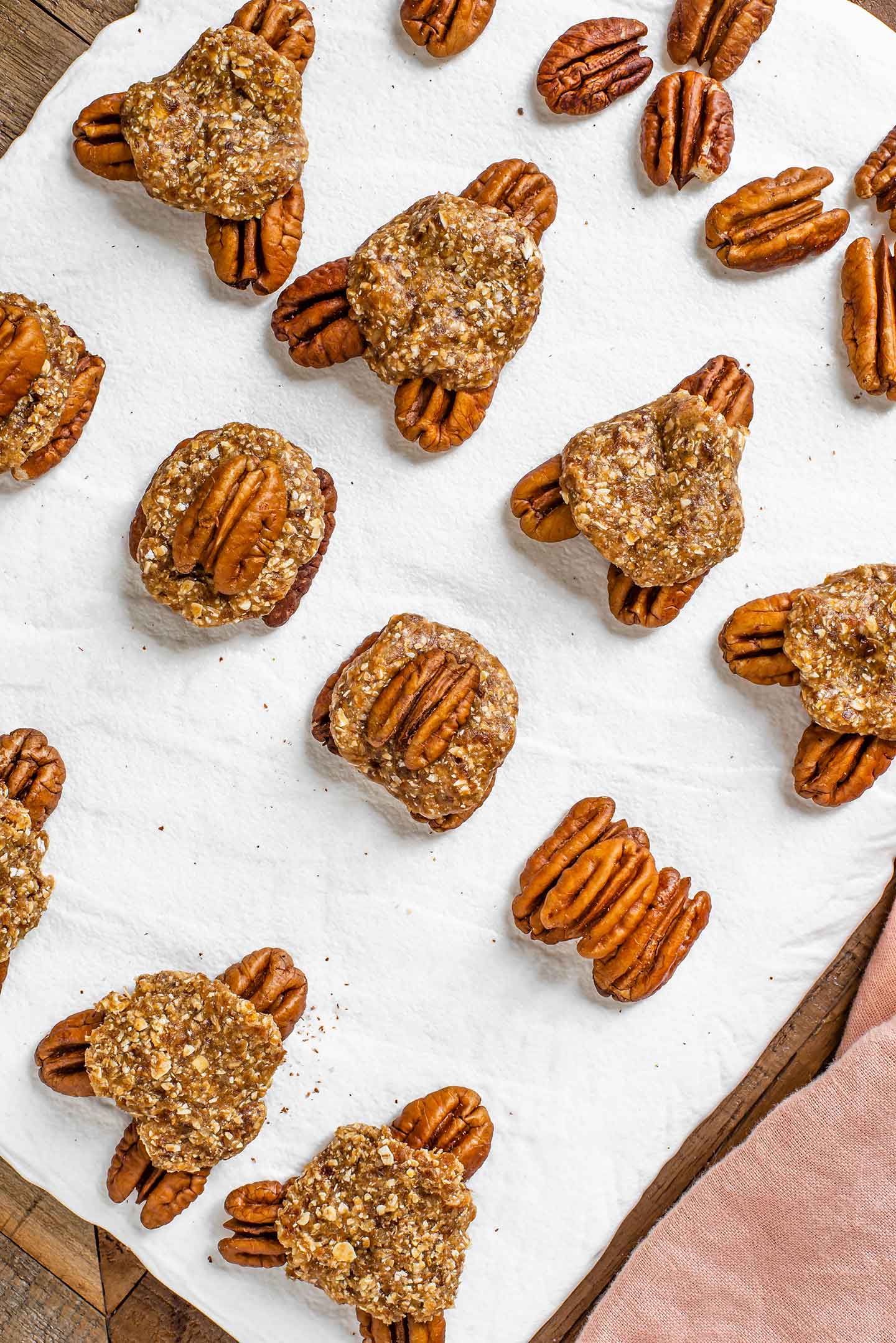 Top down view of pecans topped with date caramel patties arranged on a baking tray. Some of the pecans are arranged in groups of three to look like the head and  legs of a turtle.