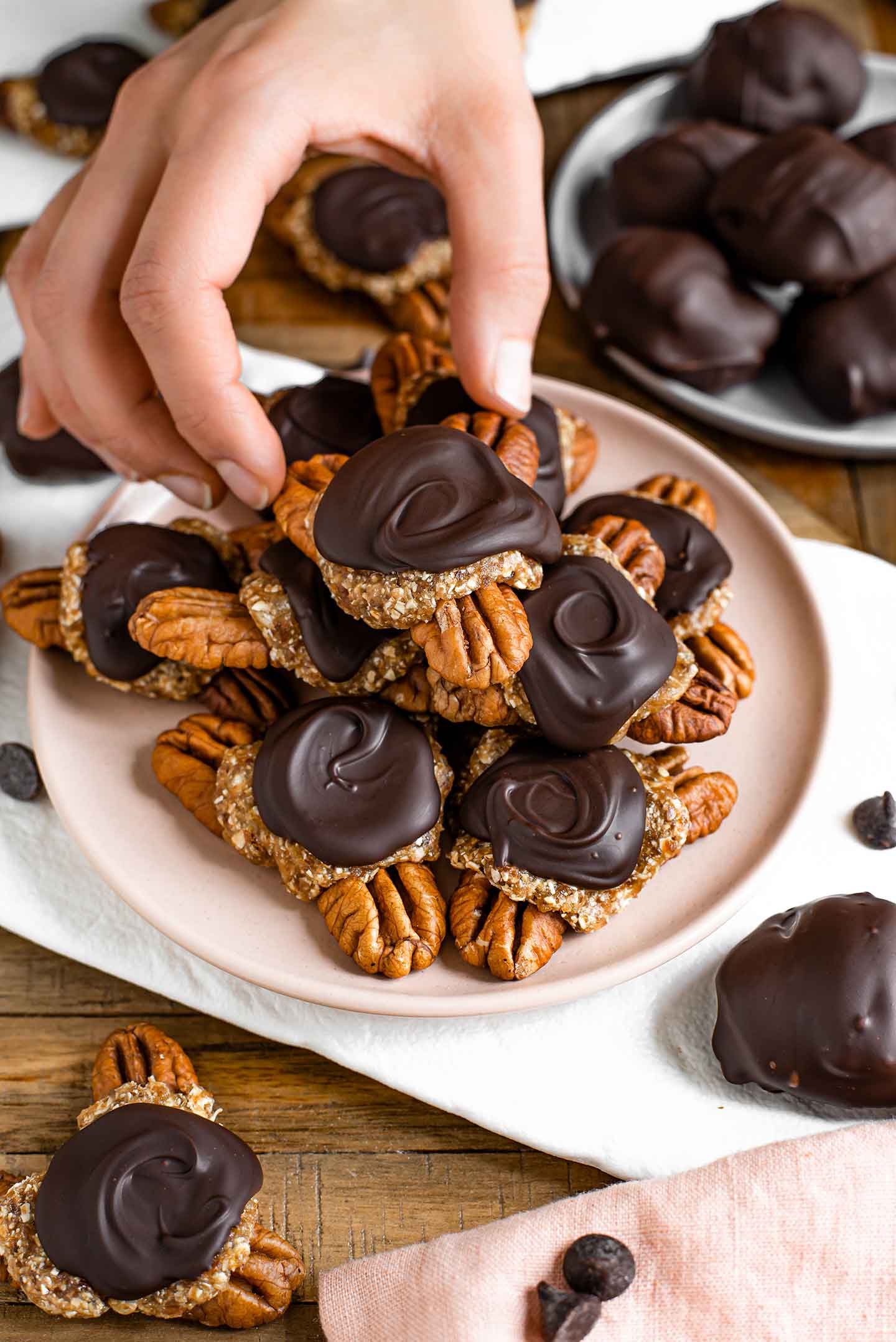 Side view of a hand reaching to grab a homemade turtles chocolate off the top of a stack of chocolates. 