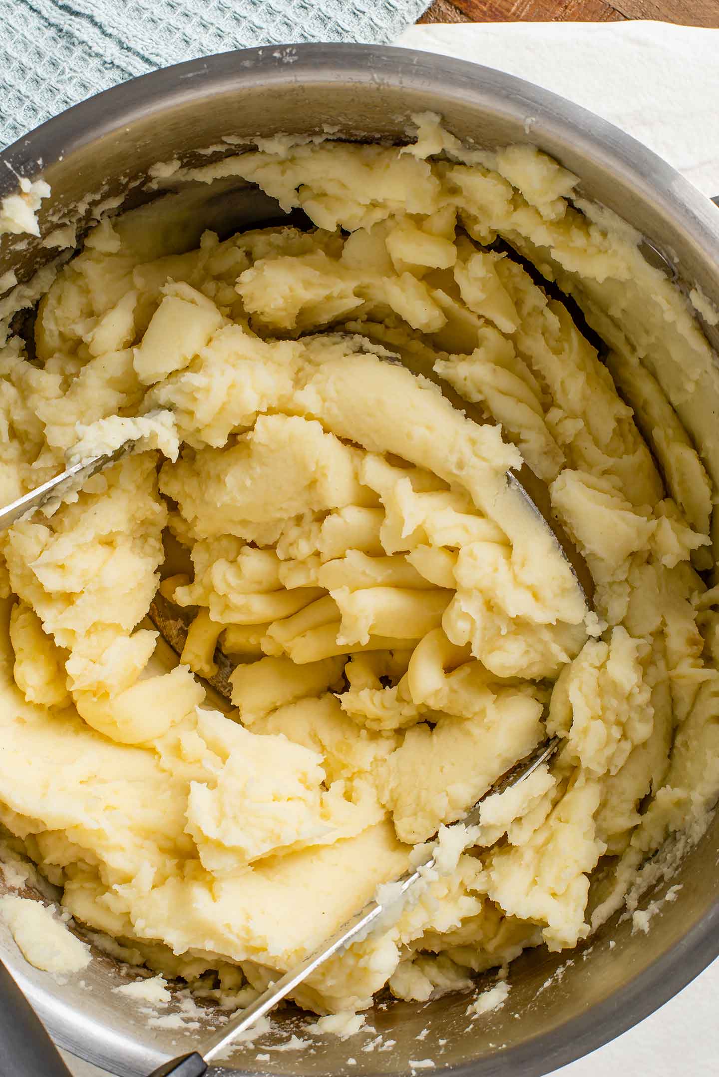 Top down view of vegan garlic mashed potatoes being mashed in a pot with a potato masher. The potatoes look fluffy and creamy.