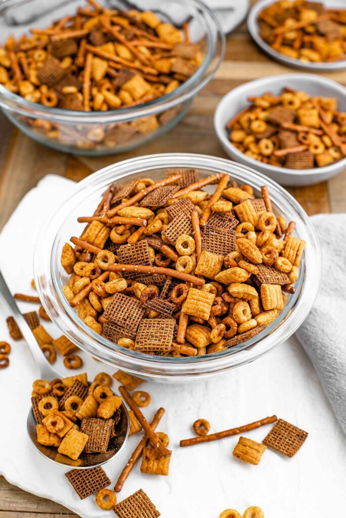 Top down view of easy vegan party mix filling a serving bowl. A spoon lays on a tray with a scoop of party mix spilling from it.