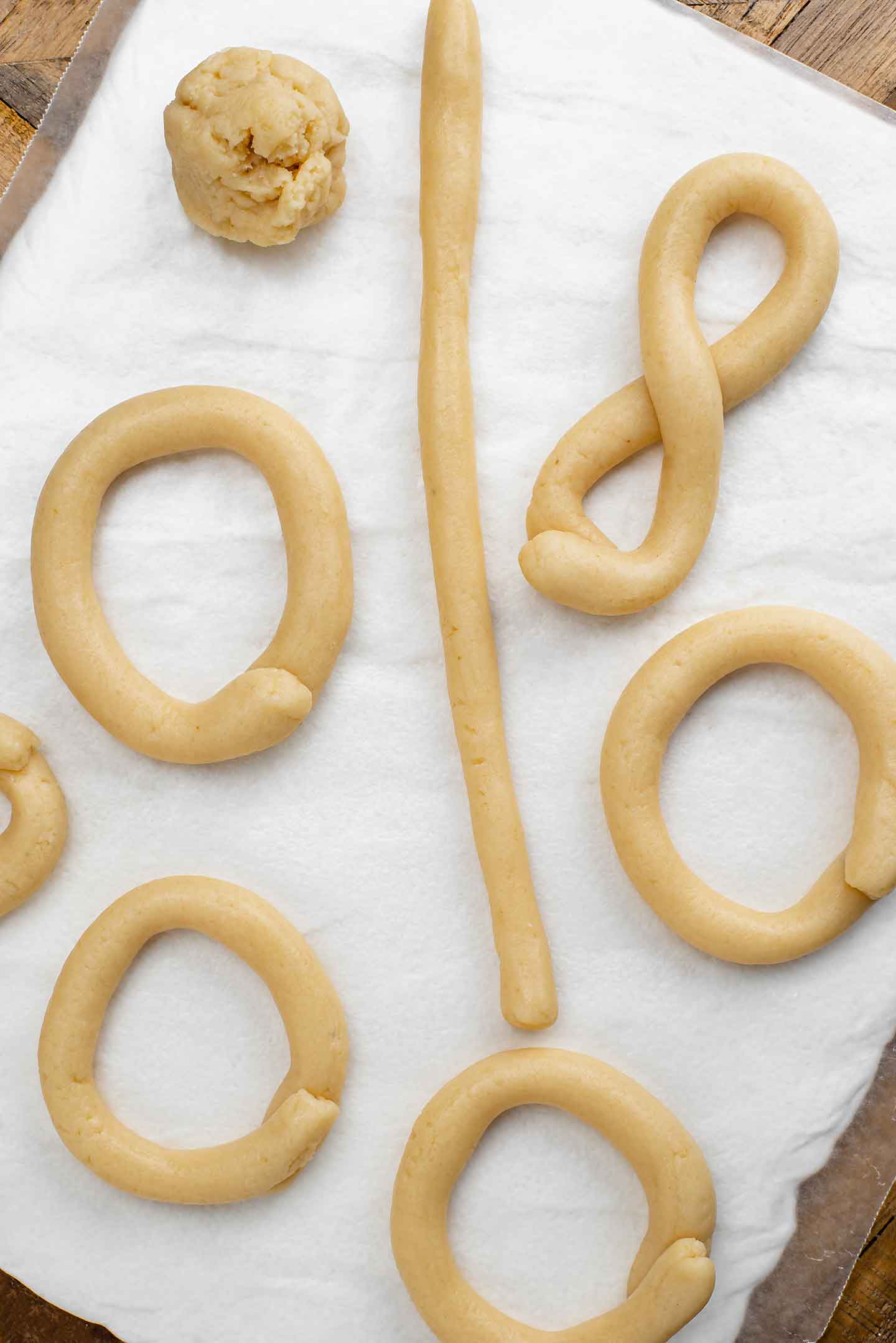 Top down view of vegan Portuguese biscoitos (cookies) being formed. Dough is first rolled into a long tubular shape and then two ends are brought together to form a circle or are twisted to create a figure eight.