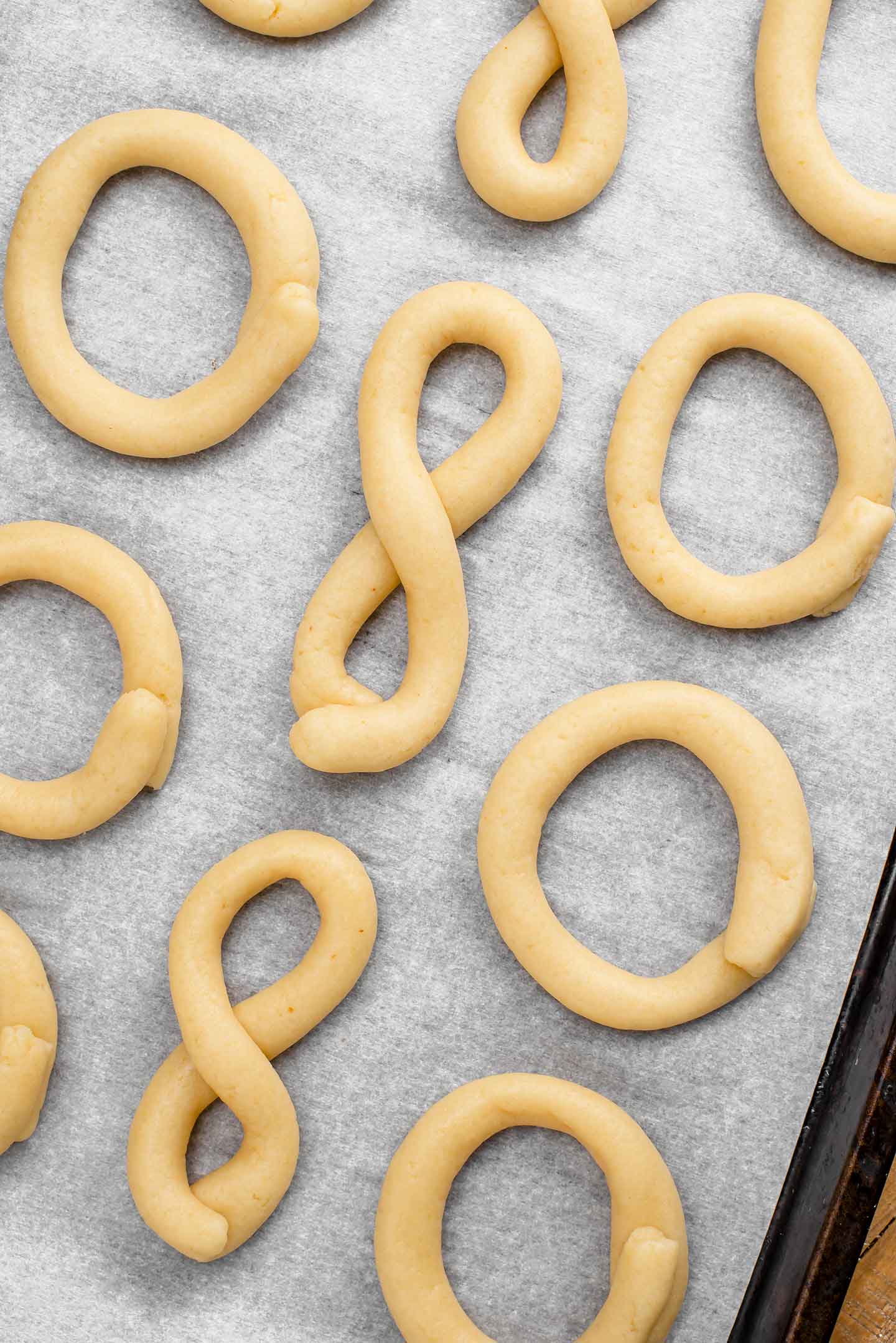 Top down view of dough on a parchment lined baking tray formed into the shape of Portuguese biscoitos and ready to go in the oven.