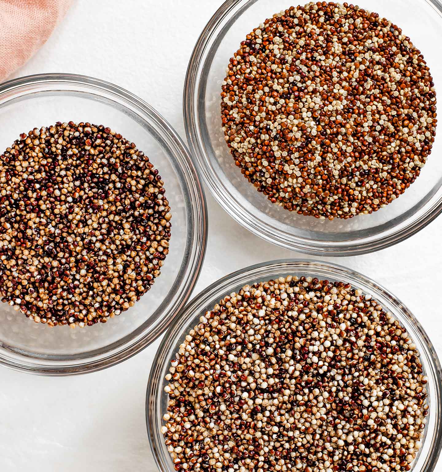 Top down view of three small bowls. In one is lightly coloured raw quinoa, in another is very dark quinoa, and in a third is lightly toasted and puffed up quinoa.