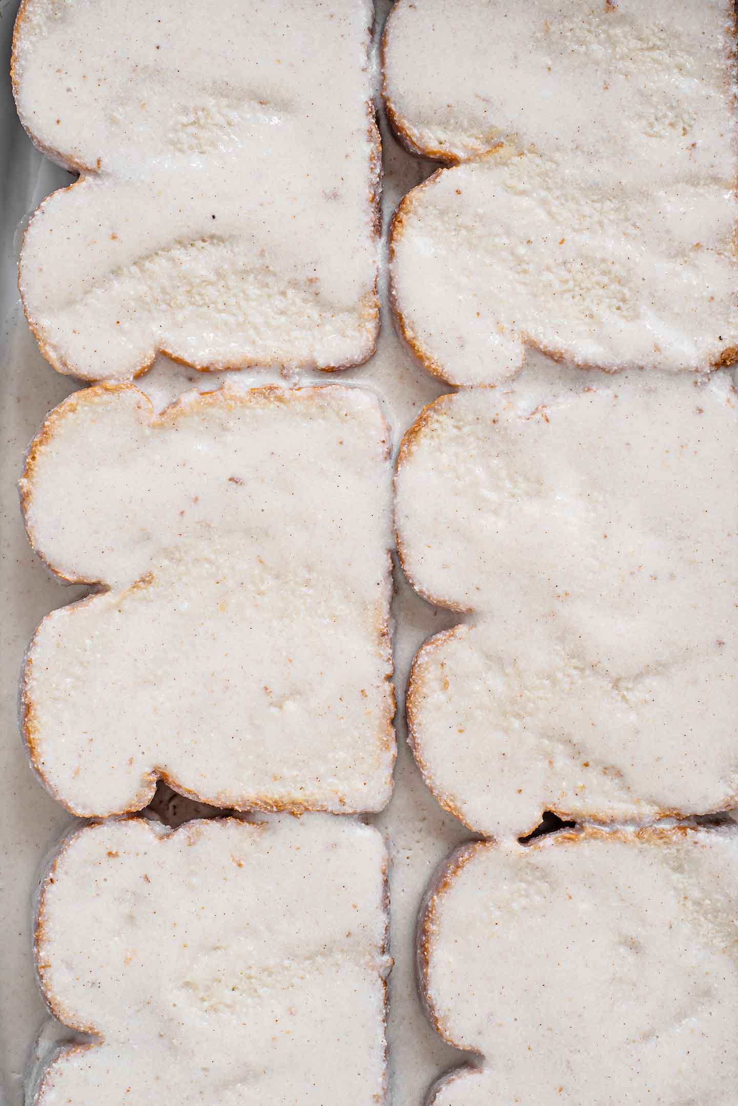 Top down view of slices of bread coated in a white custard evenly displayed in a ceramic casserole dish.