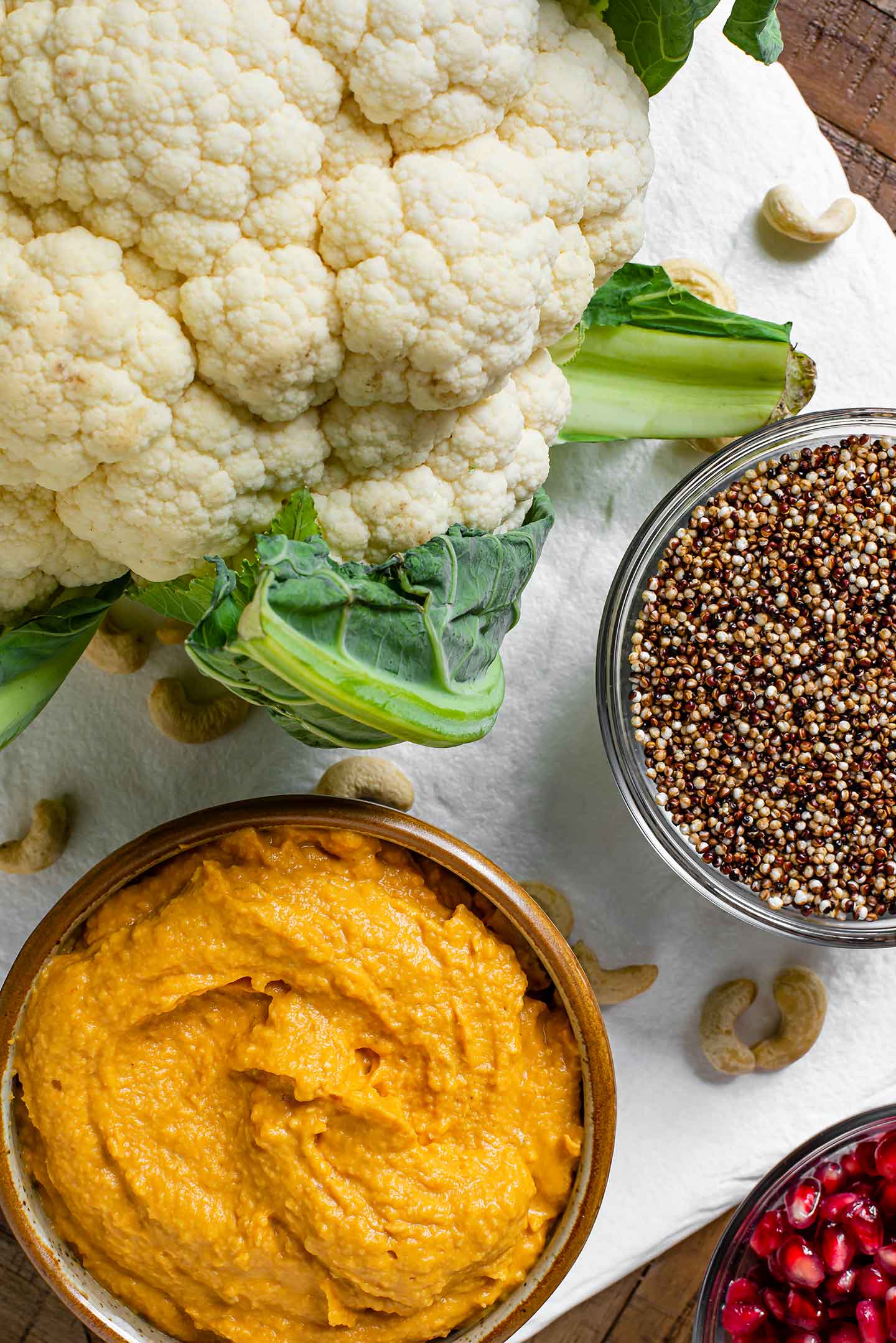 Top down view of a raw cauliflower, a bowl of popped quinoa, and a bowl of pumpkin hummus.