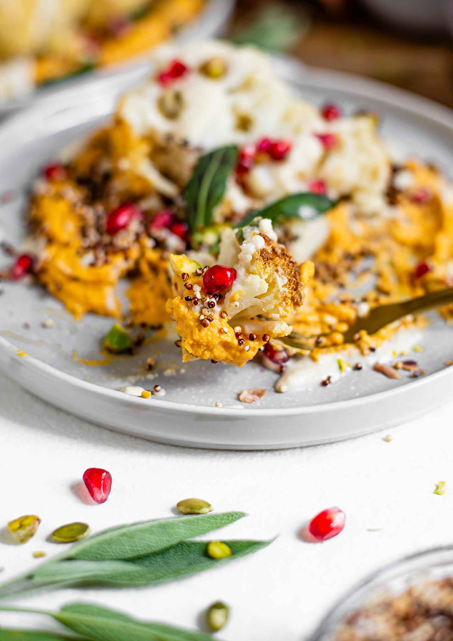 An extreme close-up of a fork holding a scoop of roasted cauliflower with some hummus, popped quinoa, and pomegranate. A tasty bite!