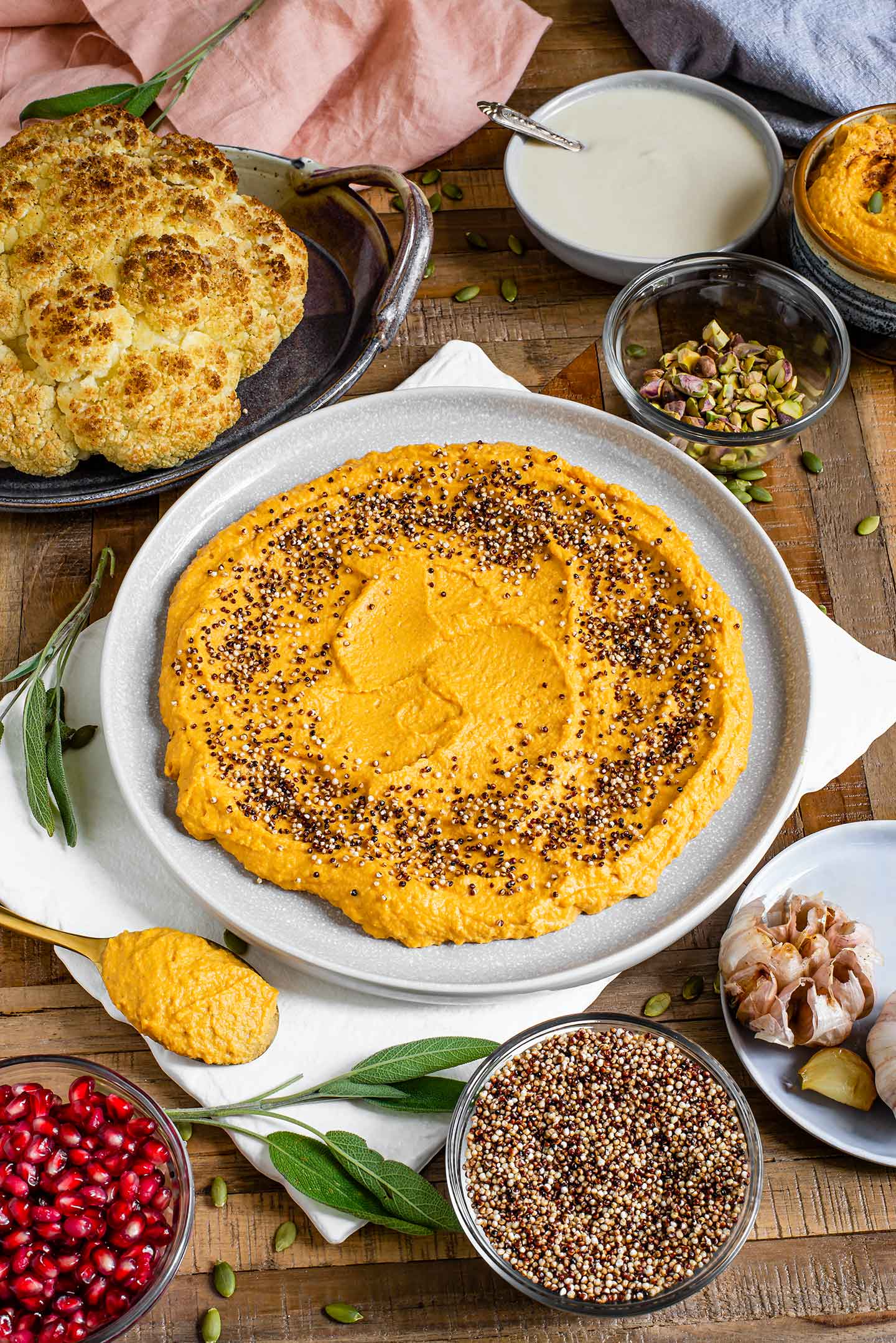 Top down view of creamy golden coloured pumpkin hummus spread on a large plate. The hummus is sprinkled with popped quinoa. 