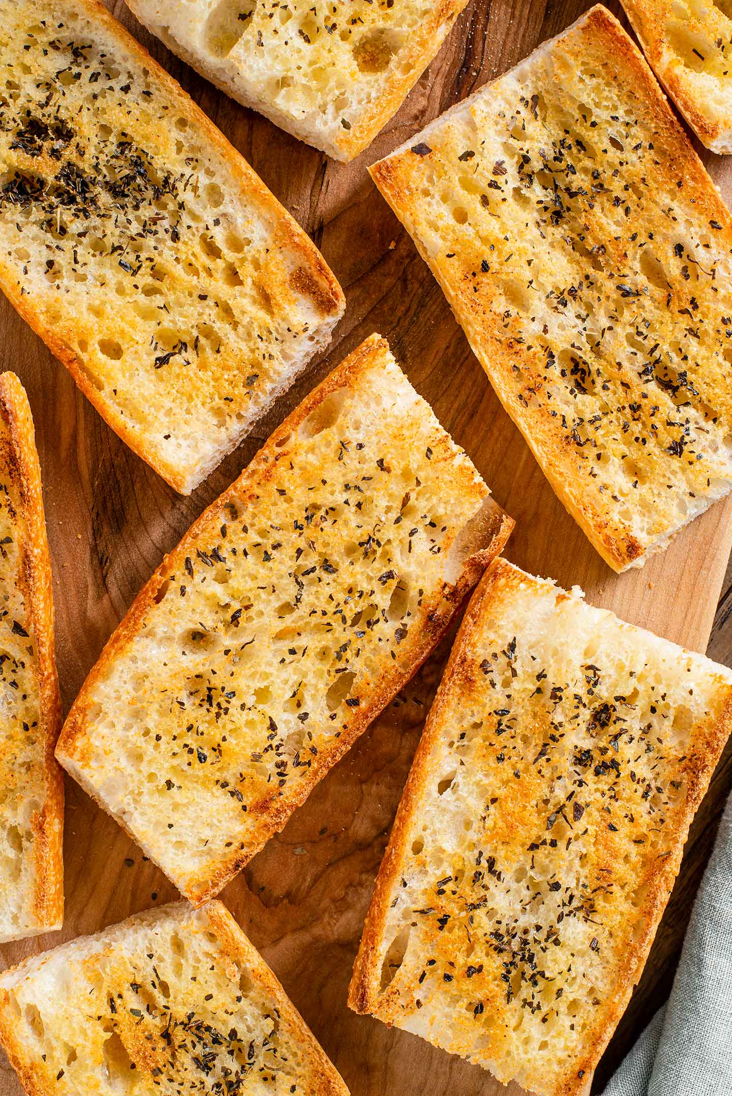 Top down view of golden slices of garlic bread on a wooden tray. The slices are sprinkled with garlic powder and dried basil.