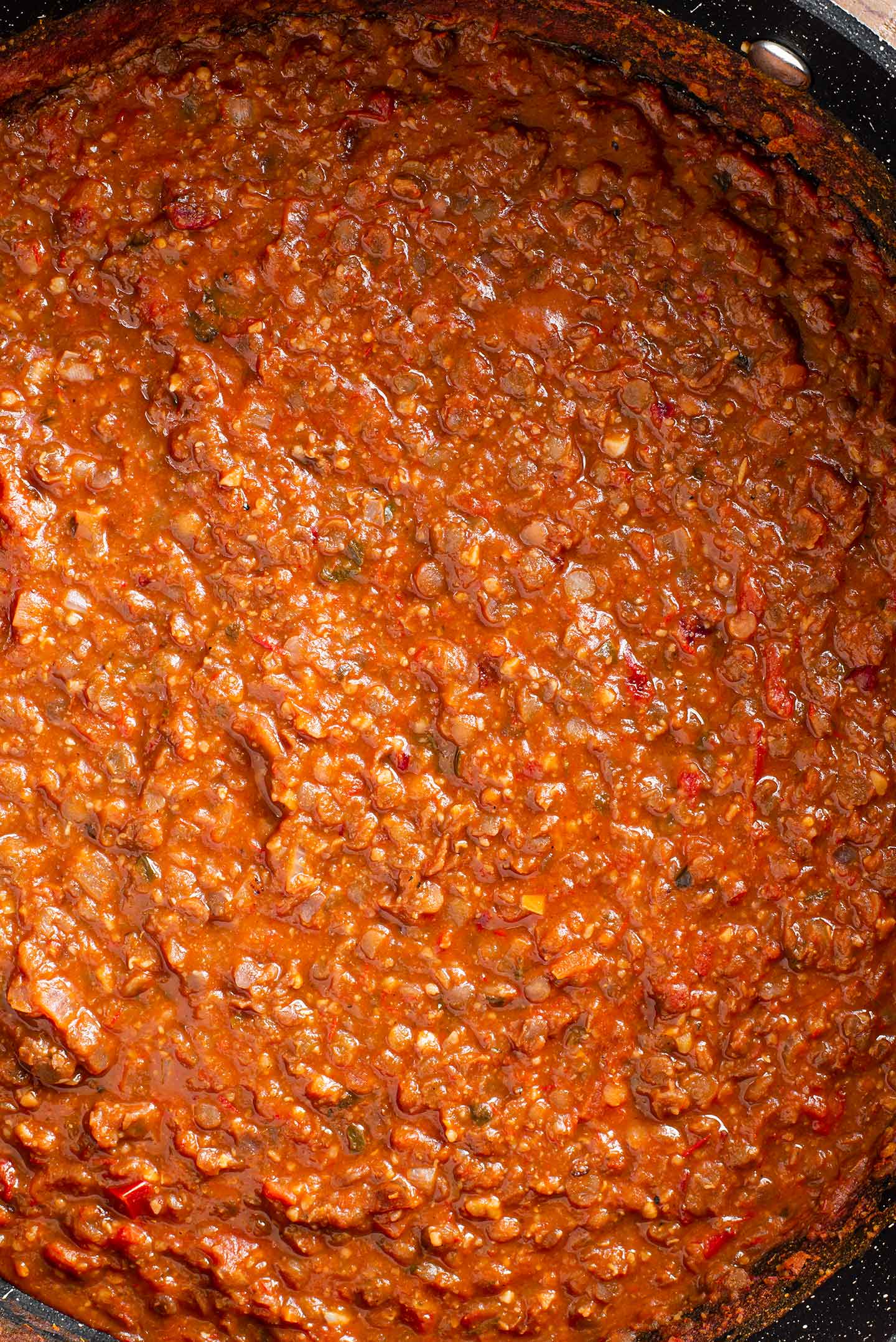 Top down view of the finished red lentil vegan "ragu" in the saute pan. The sauce is a warm red colour and has a hearty texture.