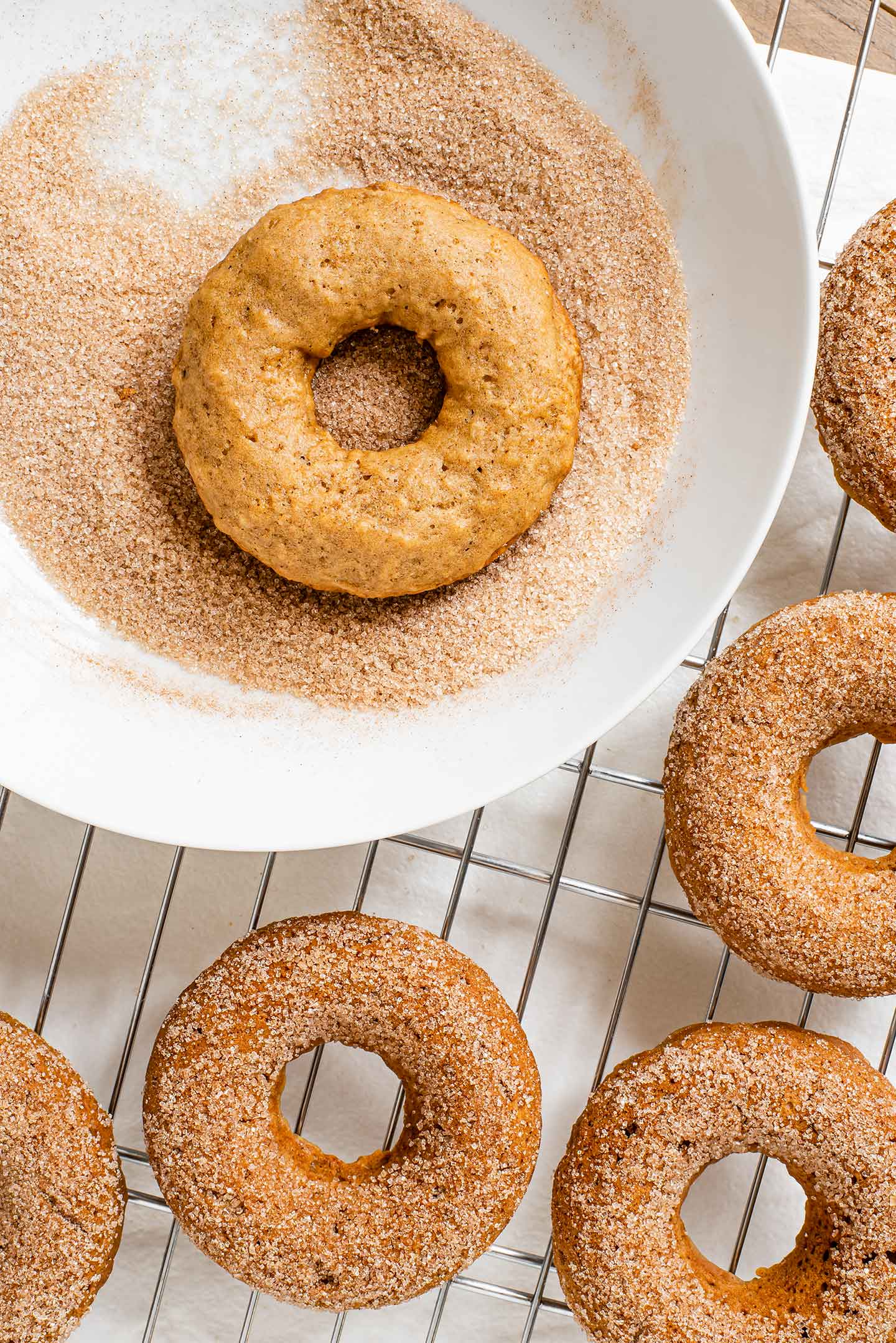 Top down view of baked doughnuts being dipped in cinnamon sugar while they are still warm.