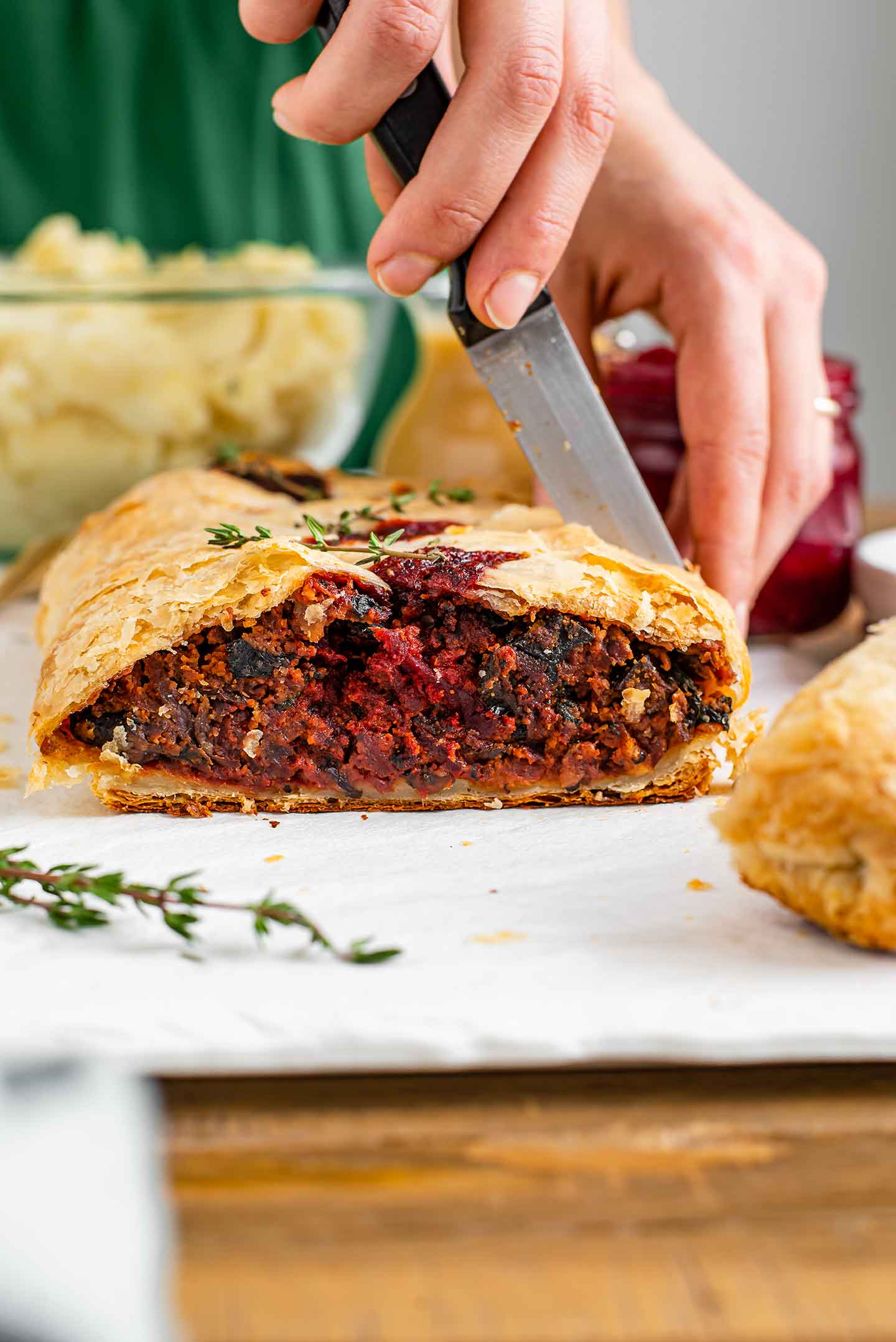 Side view of a beet wellington sliced into. Inside the flaky pastry shell is a savoury beet, mushroom, and spinach filling. The filling is compact and almost meat-like in texture.