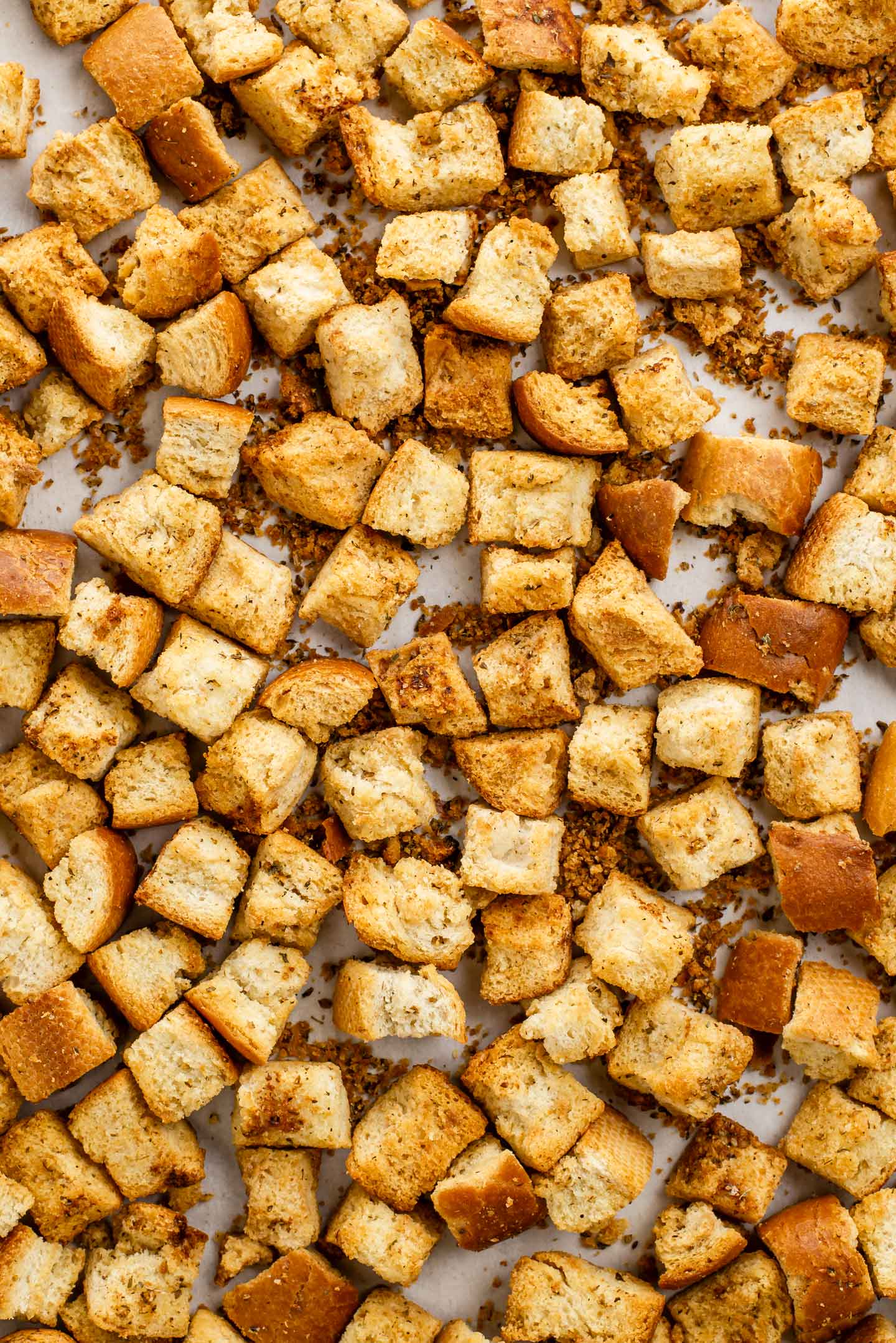 Top down view of crispy homemade croutons in a single layer in a baking tray with parchment paper