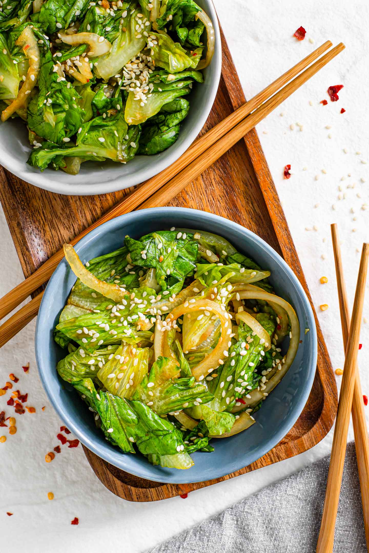 Top down view of a small bowl of a quick lettuce "kimchi" style salad. The lettuce and onions are topped with sesame seeds and chopsticks garnish the side of the tray.