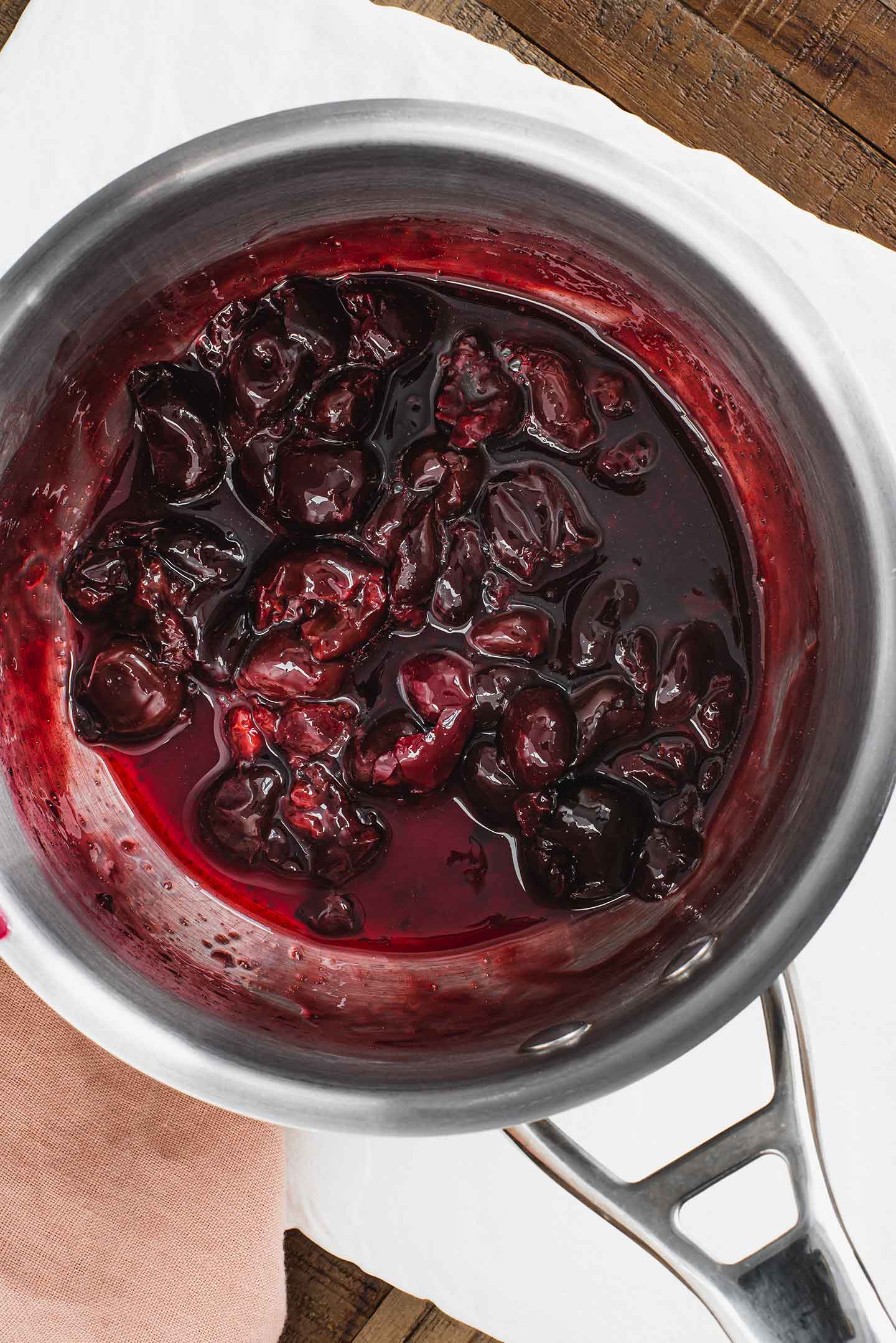 Top down view of a thickened cherry sauce in a small pot. The cherries are lightly crushed and the sauce is a deep purple colour.