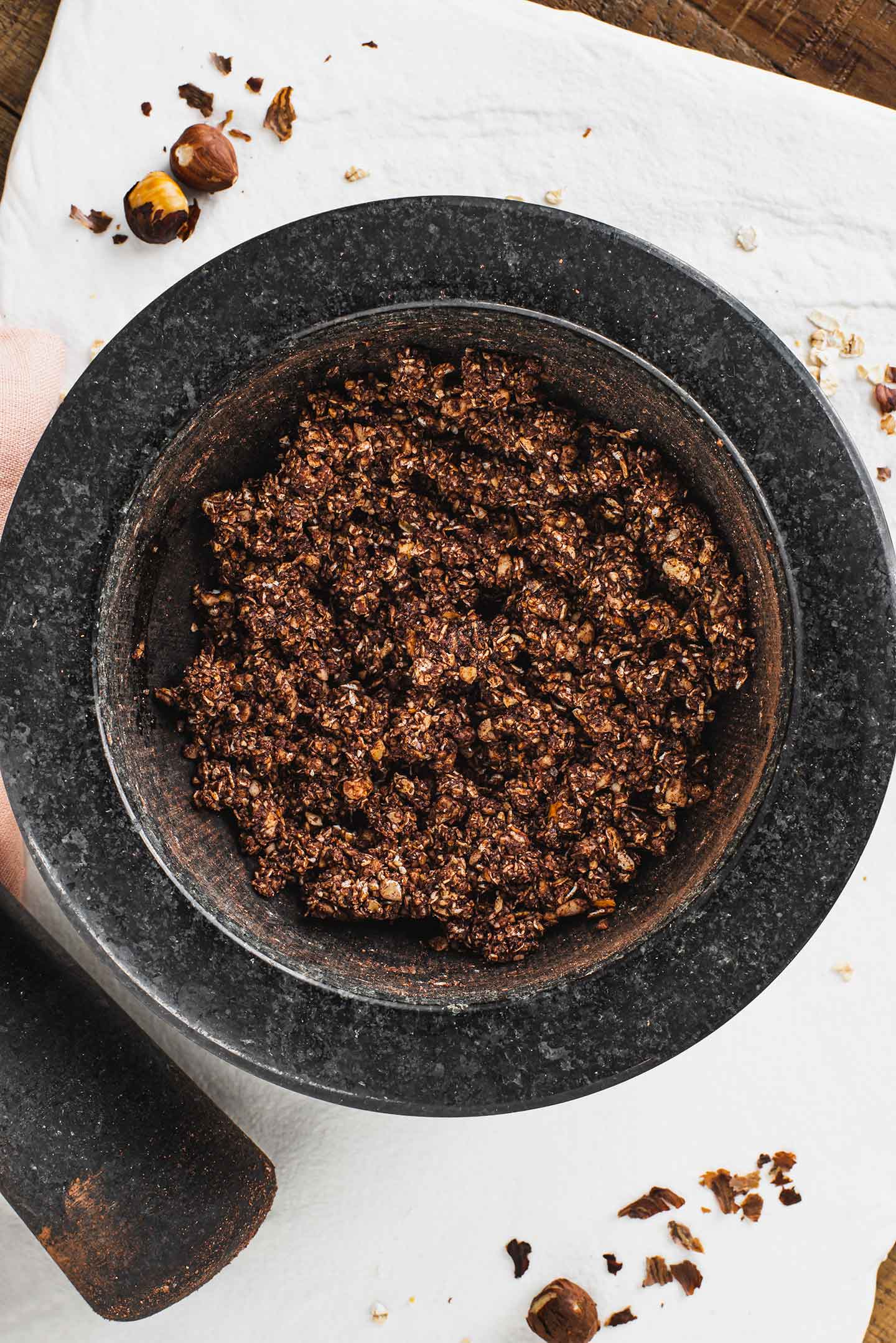 Top down view of a mixture of oats, hazelnuts, and cocoa powder in a mortar and pestle.