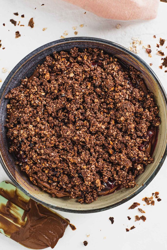 Top down view of the cookie crumble added to the top of the dessert in a shallow serving dish. The cherry sauce and chocolate mousse are just visible along the edges.