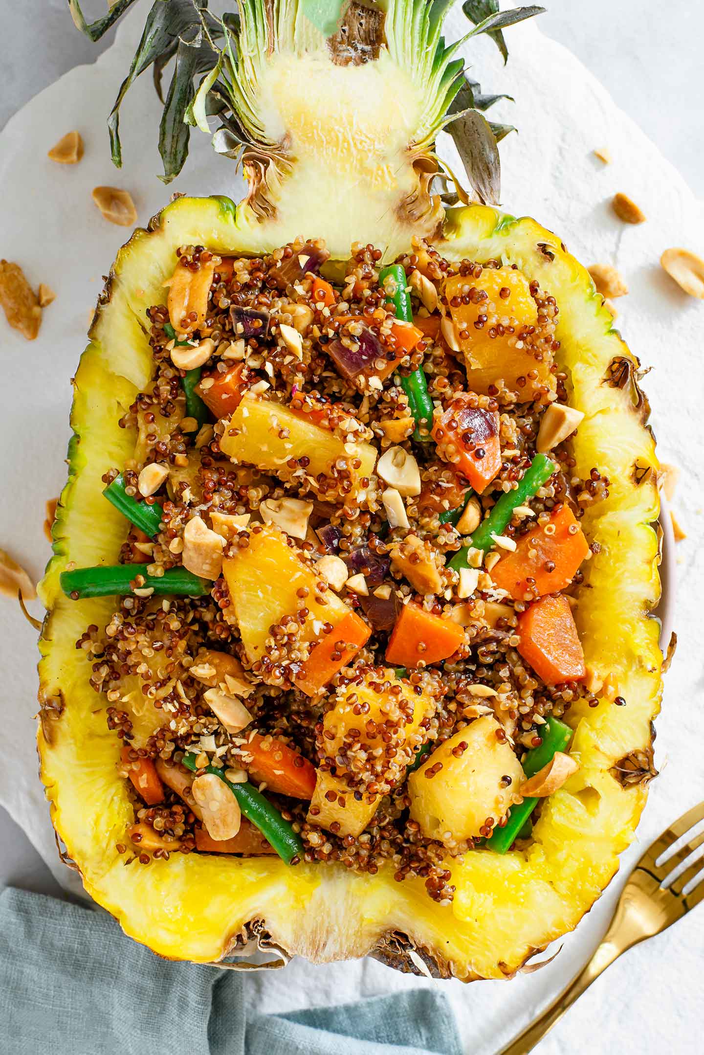 Top down view of a halved pineapple filled with quinoa, green beans, carrots, and pineapple chunks.