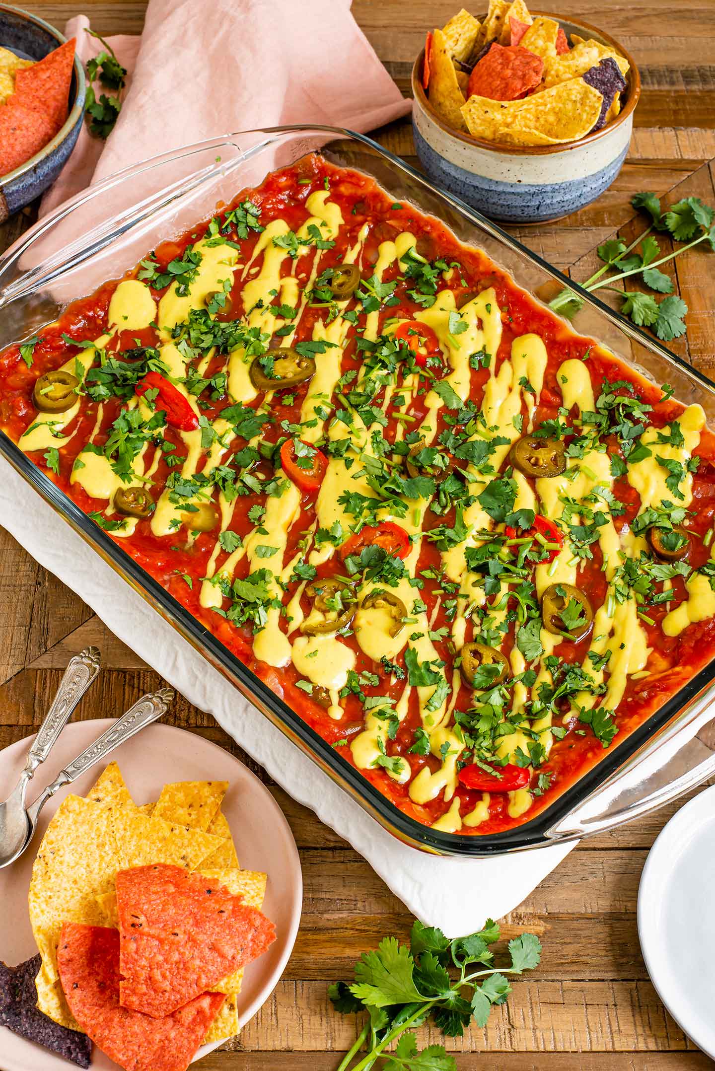 Top down view of a completed vegan 7 layer party dip ready to serve. Chips are pictured to the side of the dip.