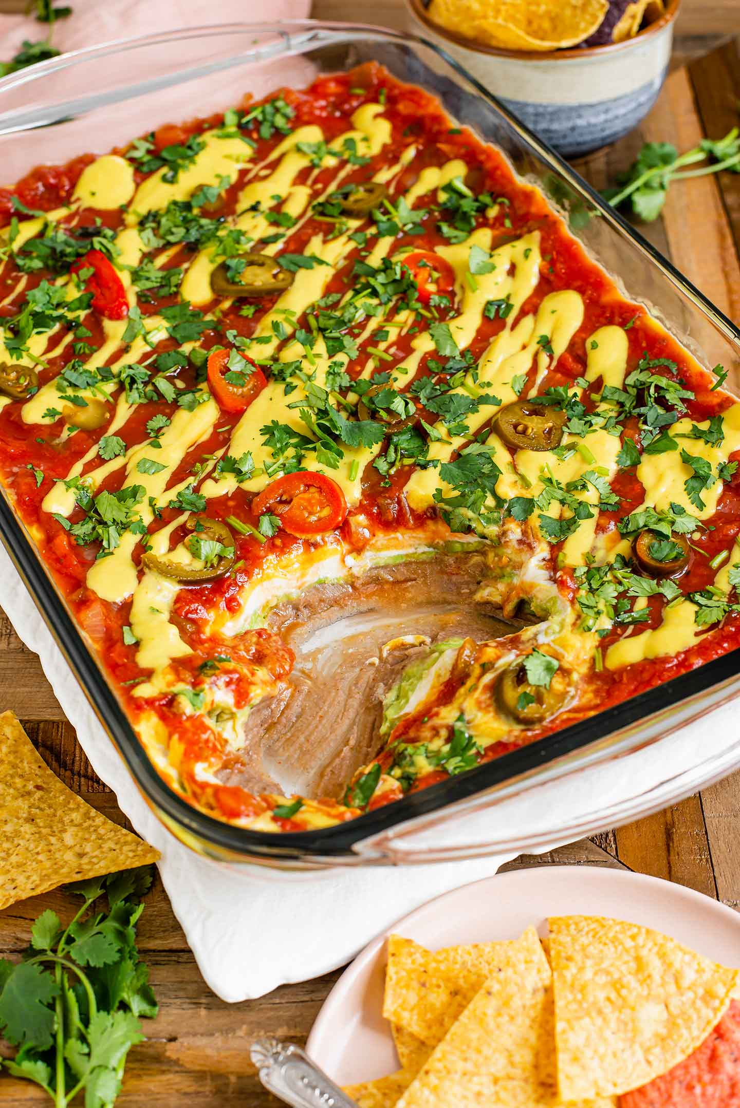 Top down view of a large rectangular dish of vegan 7 layer party dip. Some of the dip has been eaten exposing the 7 colourful layers.