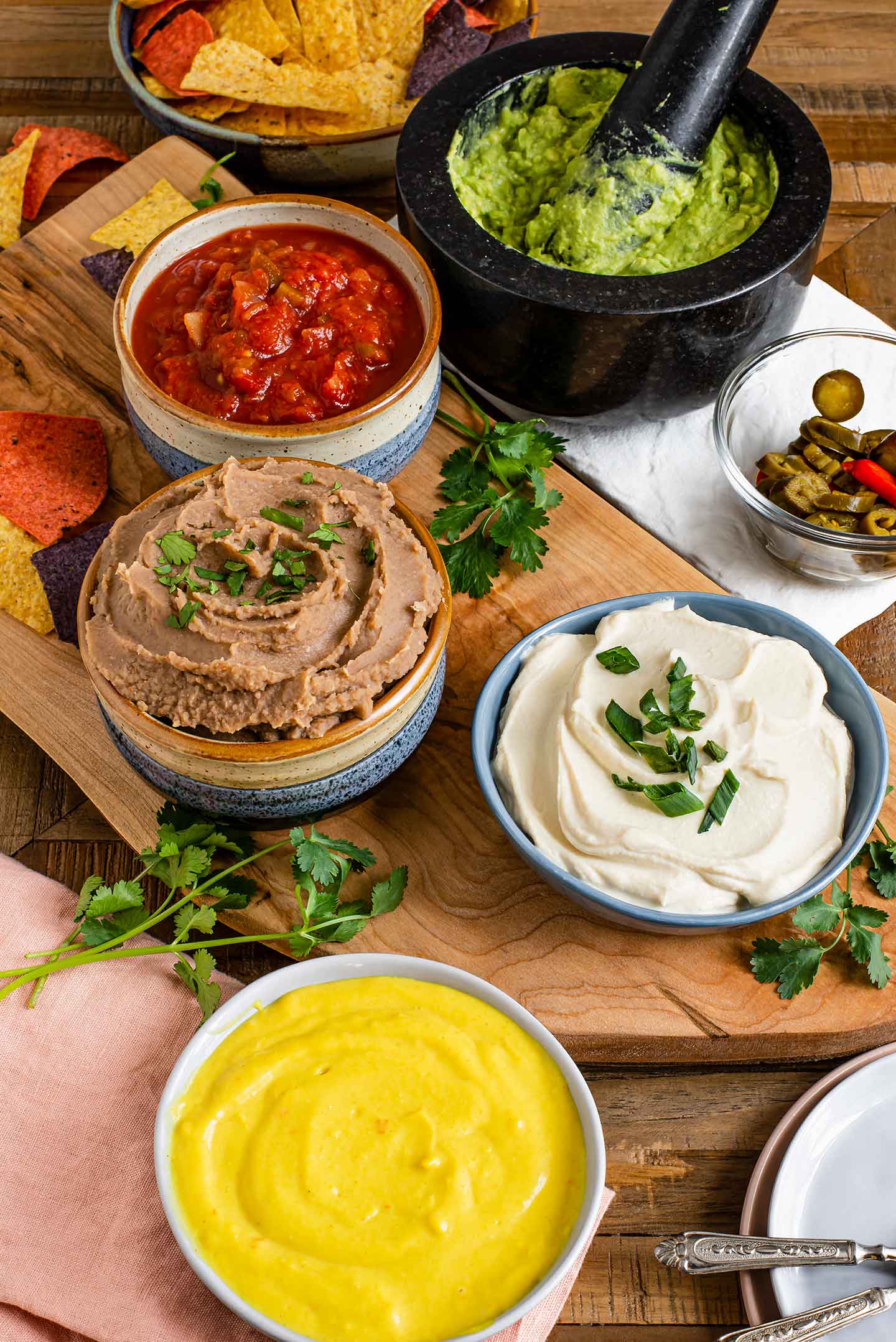 Top down view of small dishes containing each of the 5 dips. Cilantro and sliced jalapeños are among the ingredients.