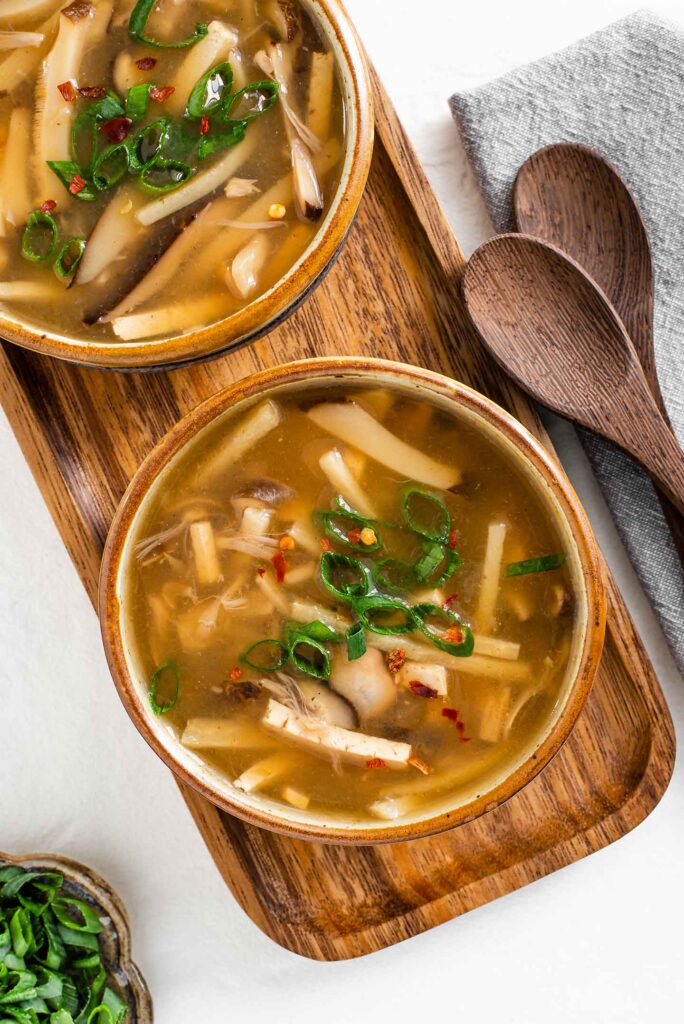 Top down view of two bowls of vegan hot and sour soup. The top of the soup is garnished with green onion.